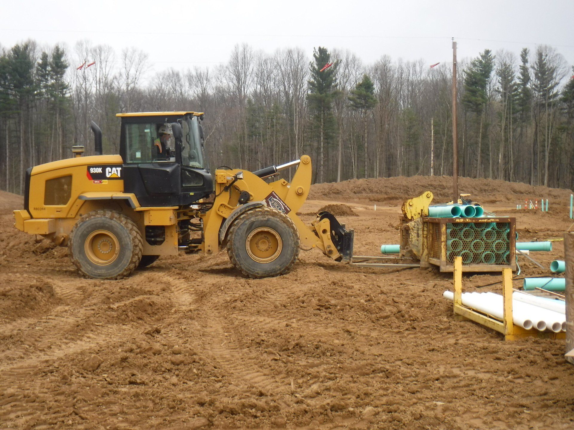 Yellow CAT loader at a construction site, moving pipes.