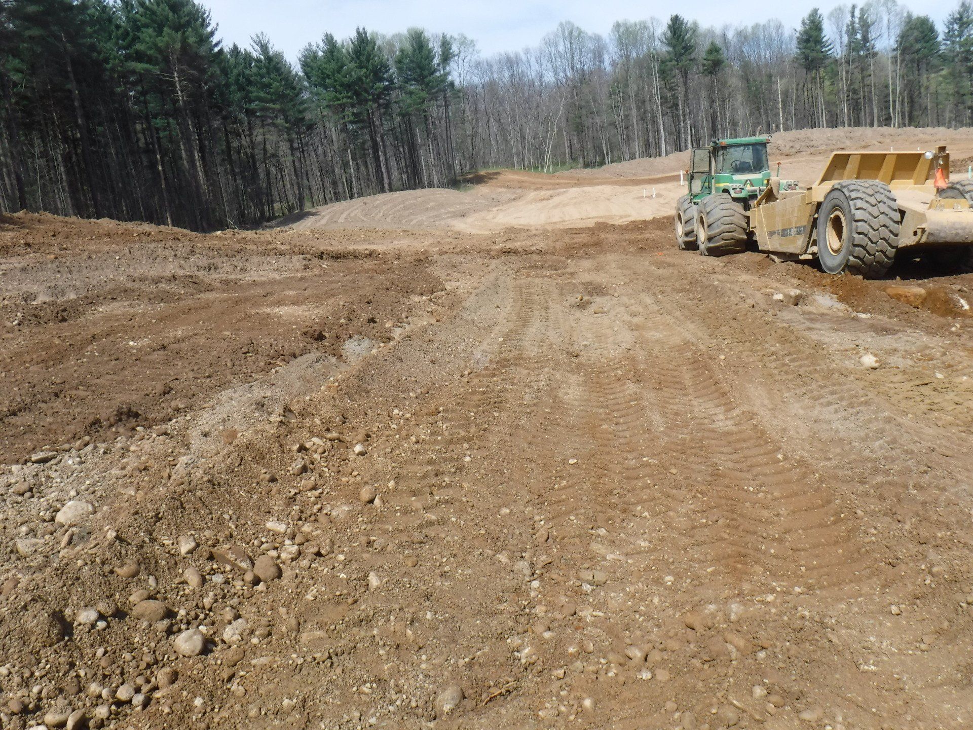 Earthmoving equipment grading a construction site with trees in the background.