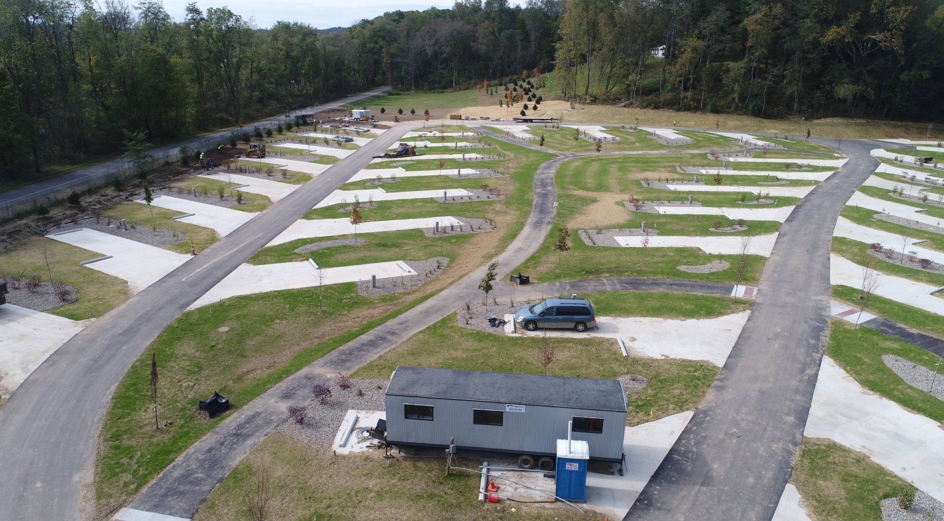 An aerial view of a campground with paved roads, RV sites, and a small, gray building.