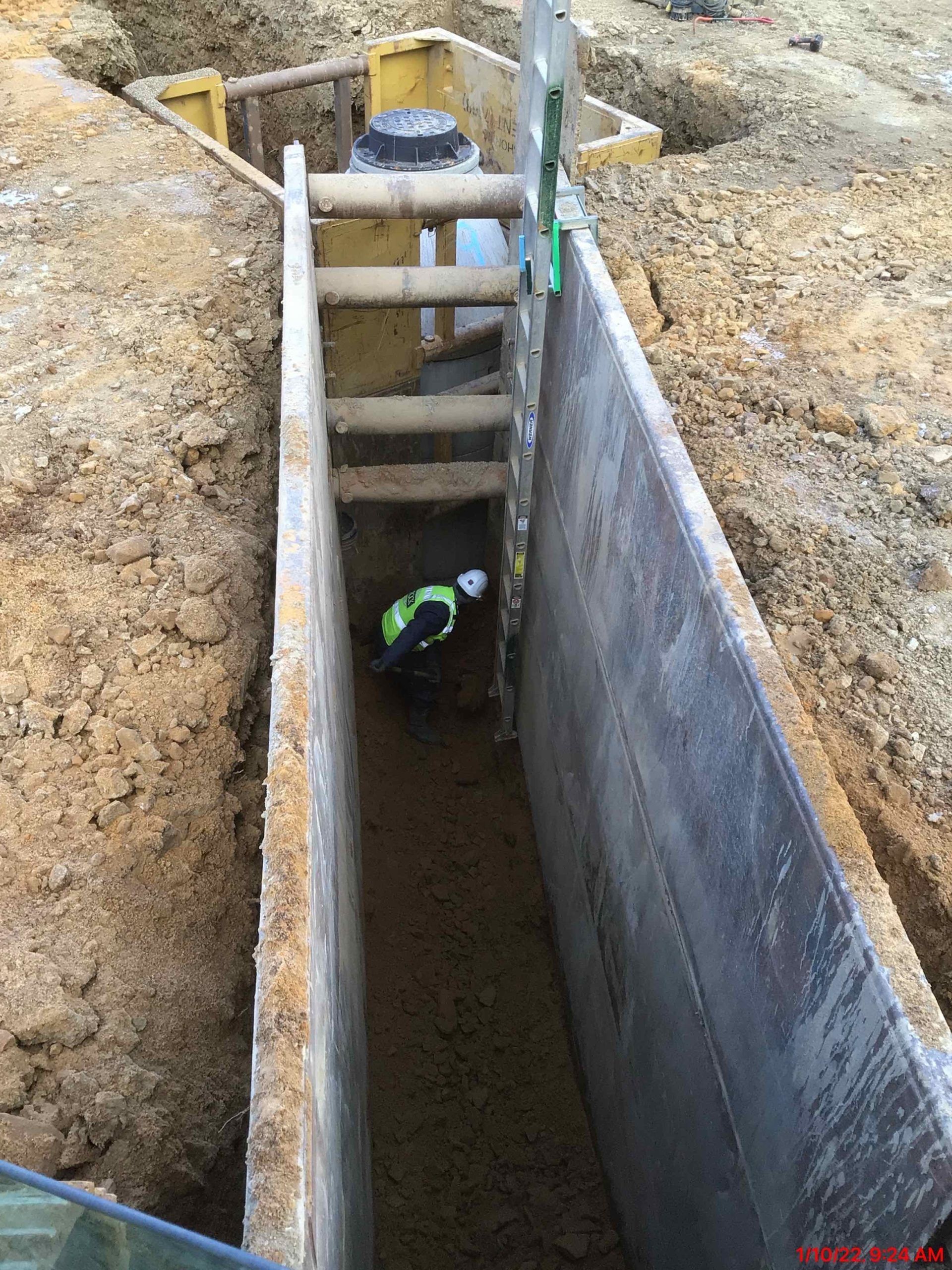 A worker in a trench with a ladder. The trench is shored up with wooden planks.