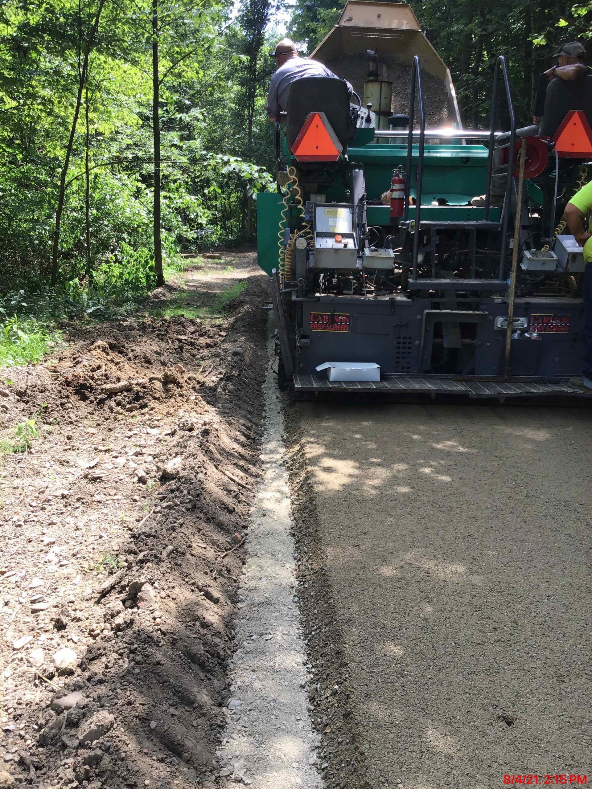 Asphalt paving machine laying down new gravel surface on a forest path.