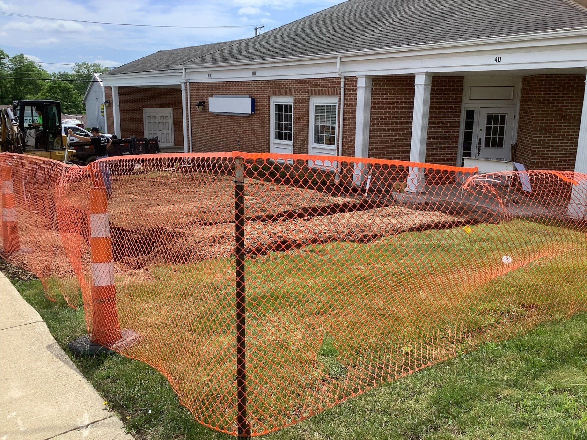 Construction site with orange safety fencing in front of a brick building. Grass is visible.