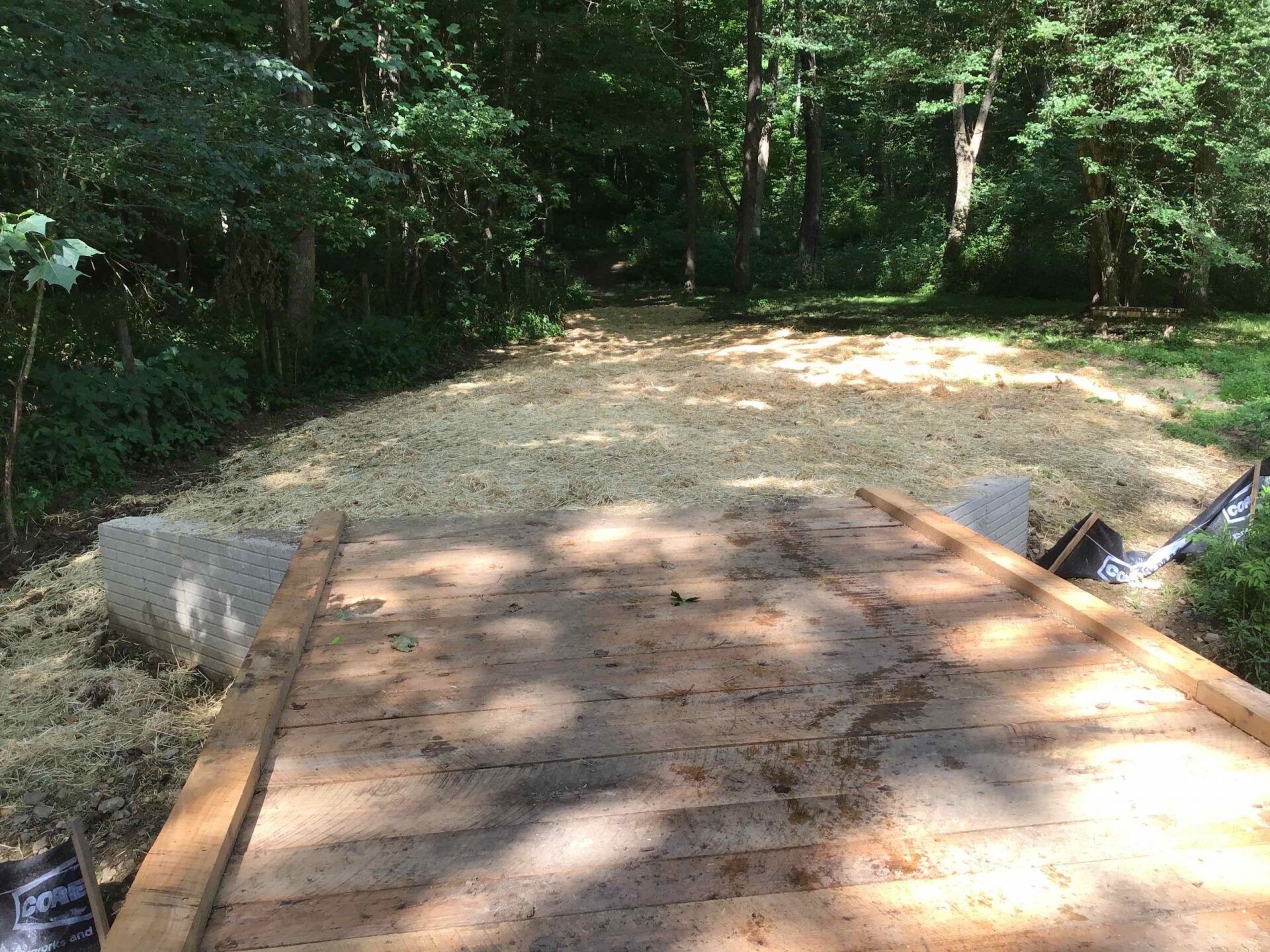 Wooden platform on concrete blocks with gravel in the background, surrounded by trees.