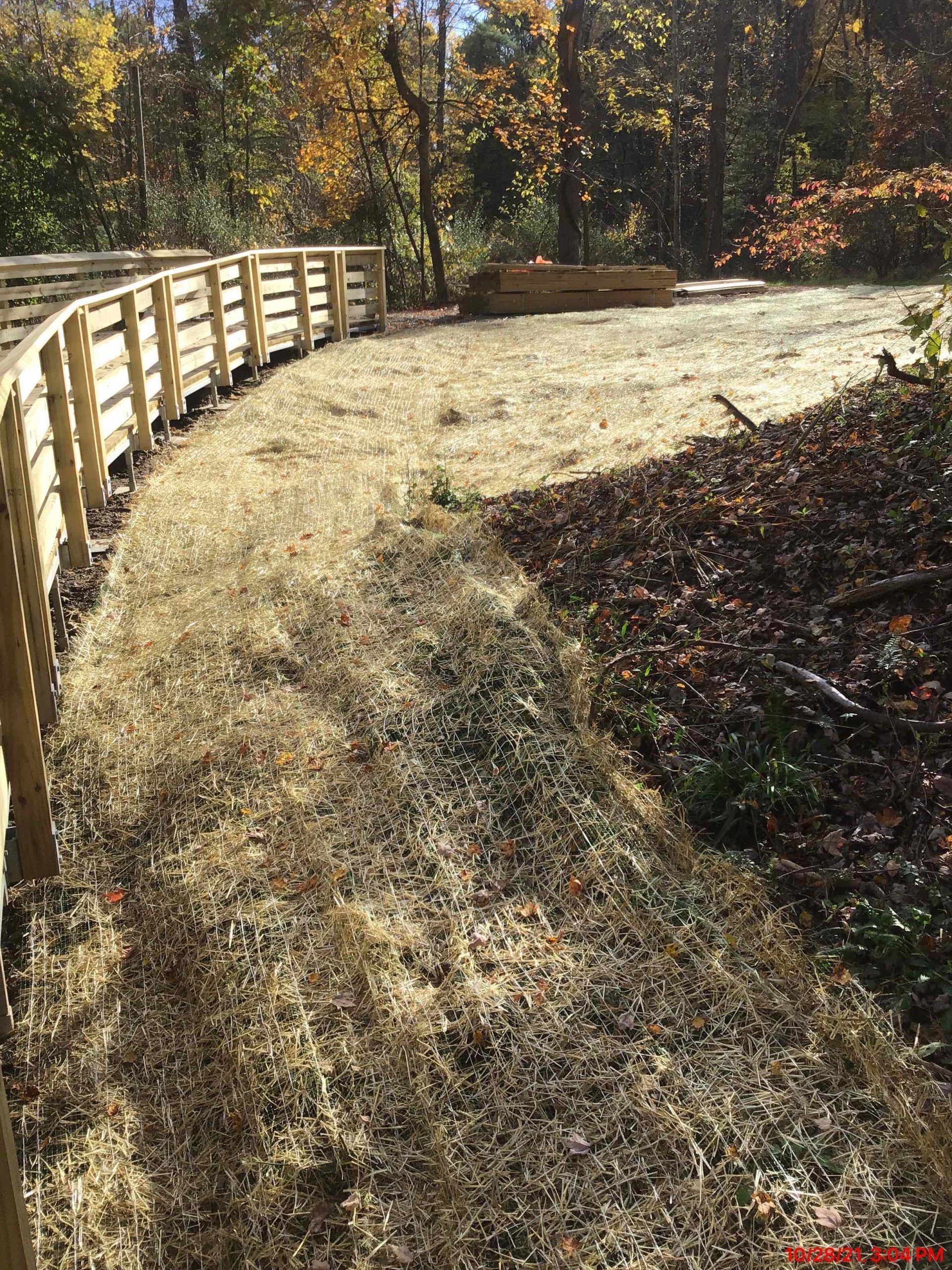 Wooden fence borders a grassy path through a wooded area.
