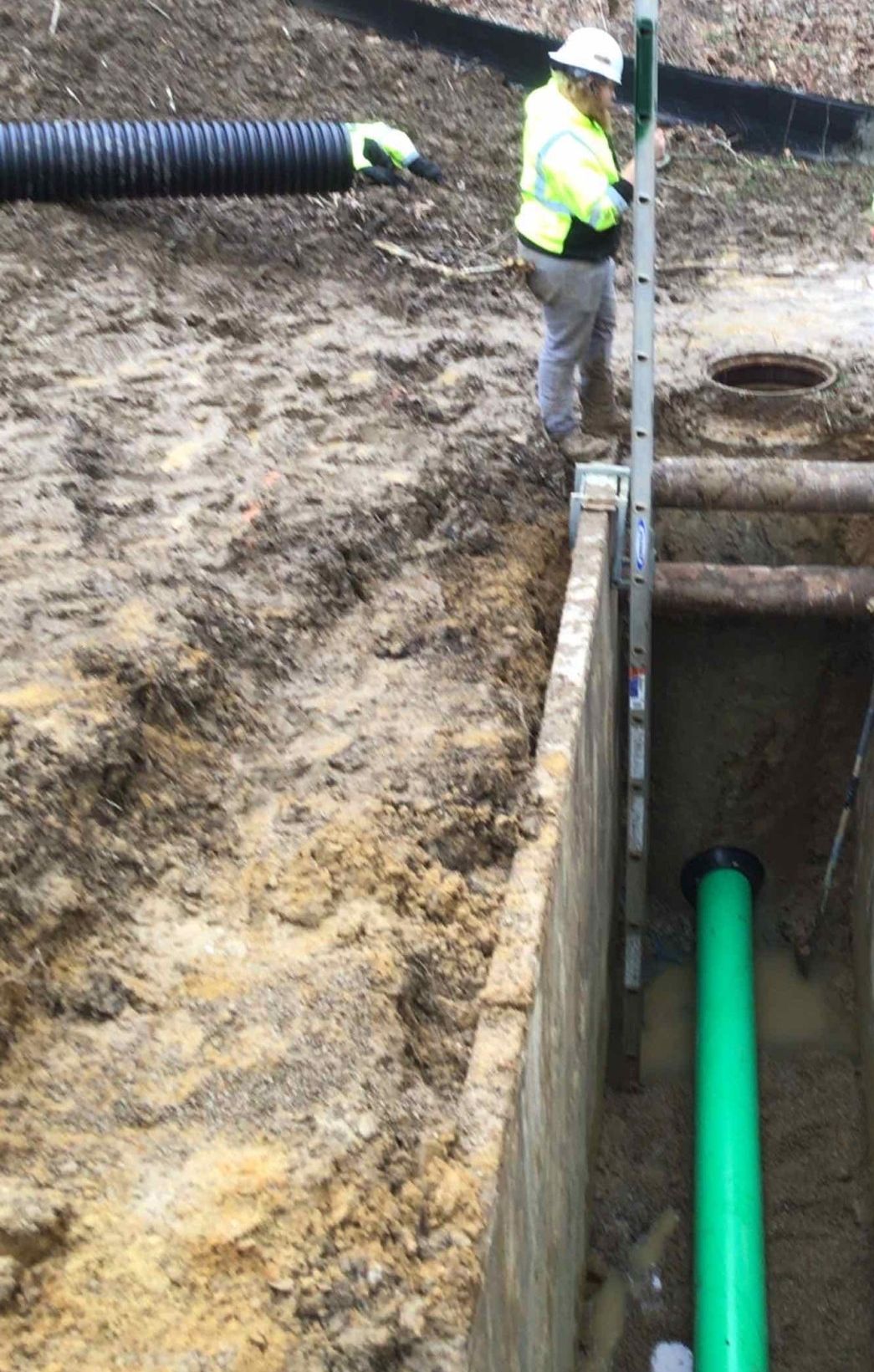 Construction worker in reflective vest, measuring the depth of a trench with green pipe.