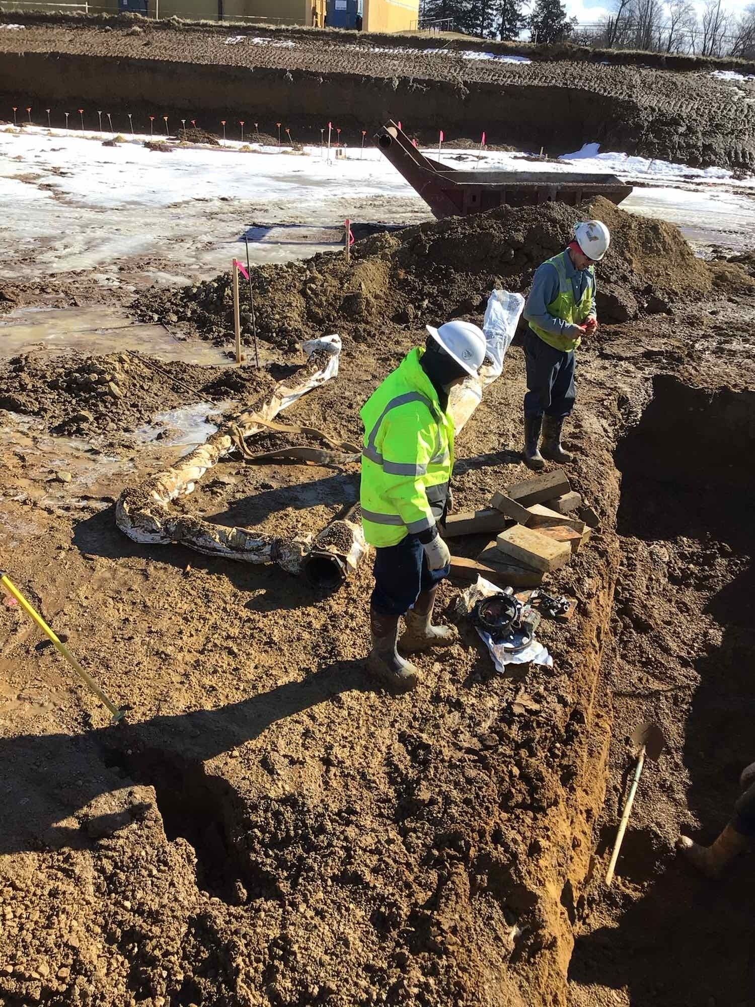 Two people in reflective vests inspect a construction site excavation.