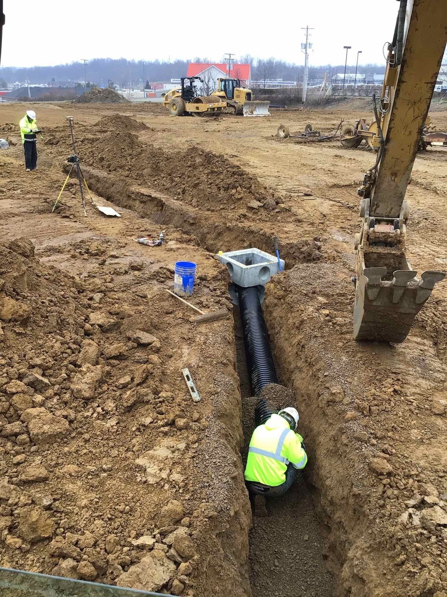 Construction workers installing drainage pipes in a trench at a muddy construction site.