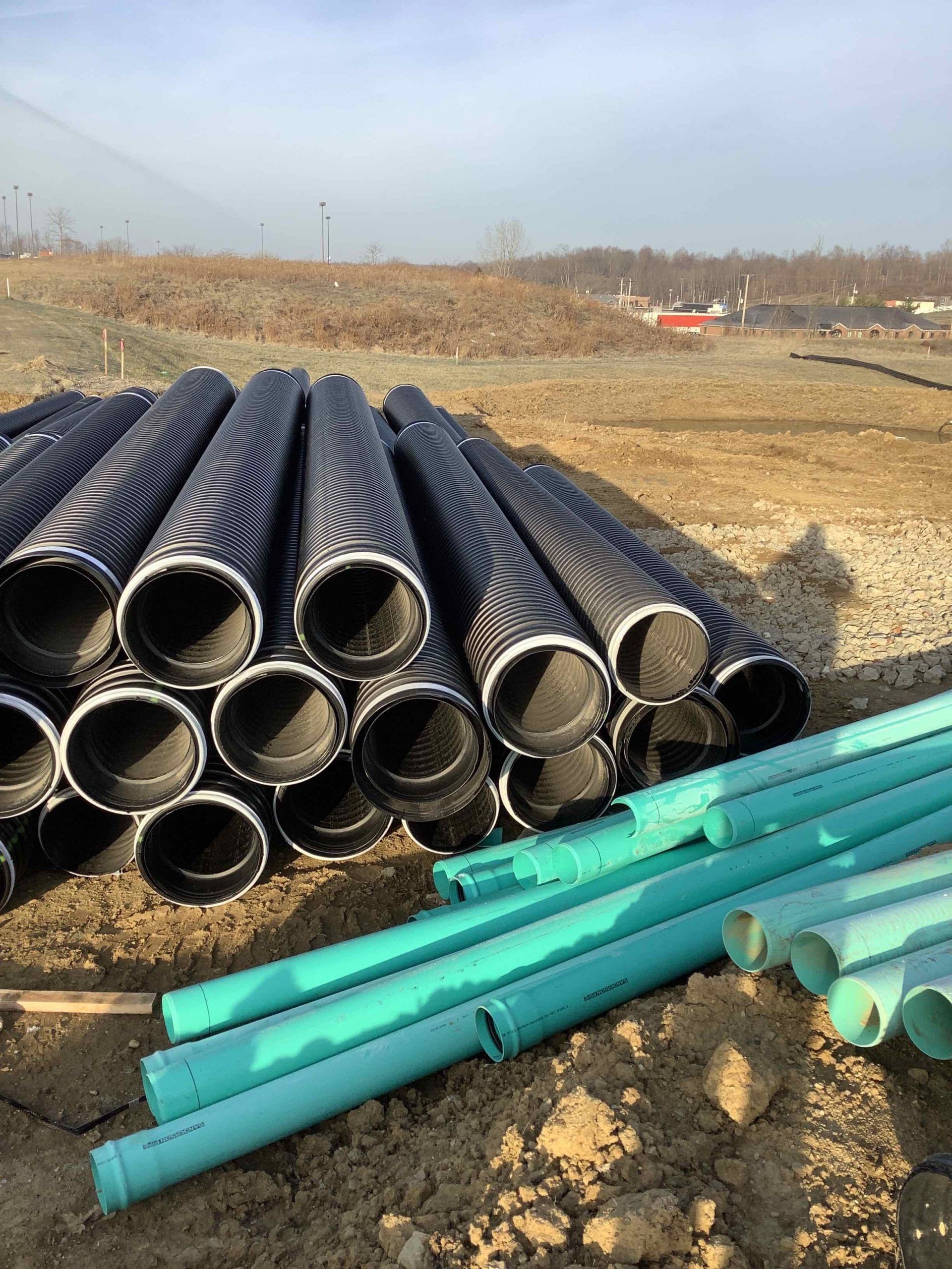 Piles of black and teal pipes on a construction site.