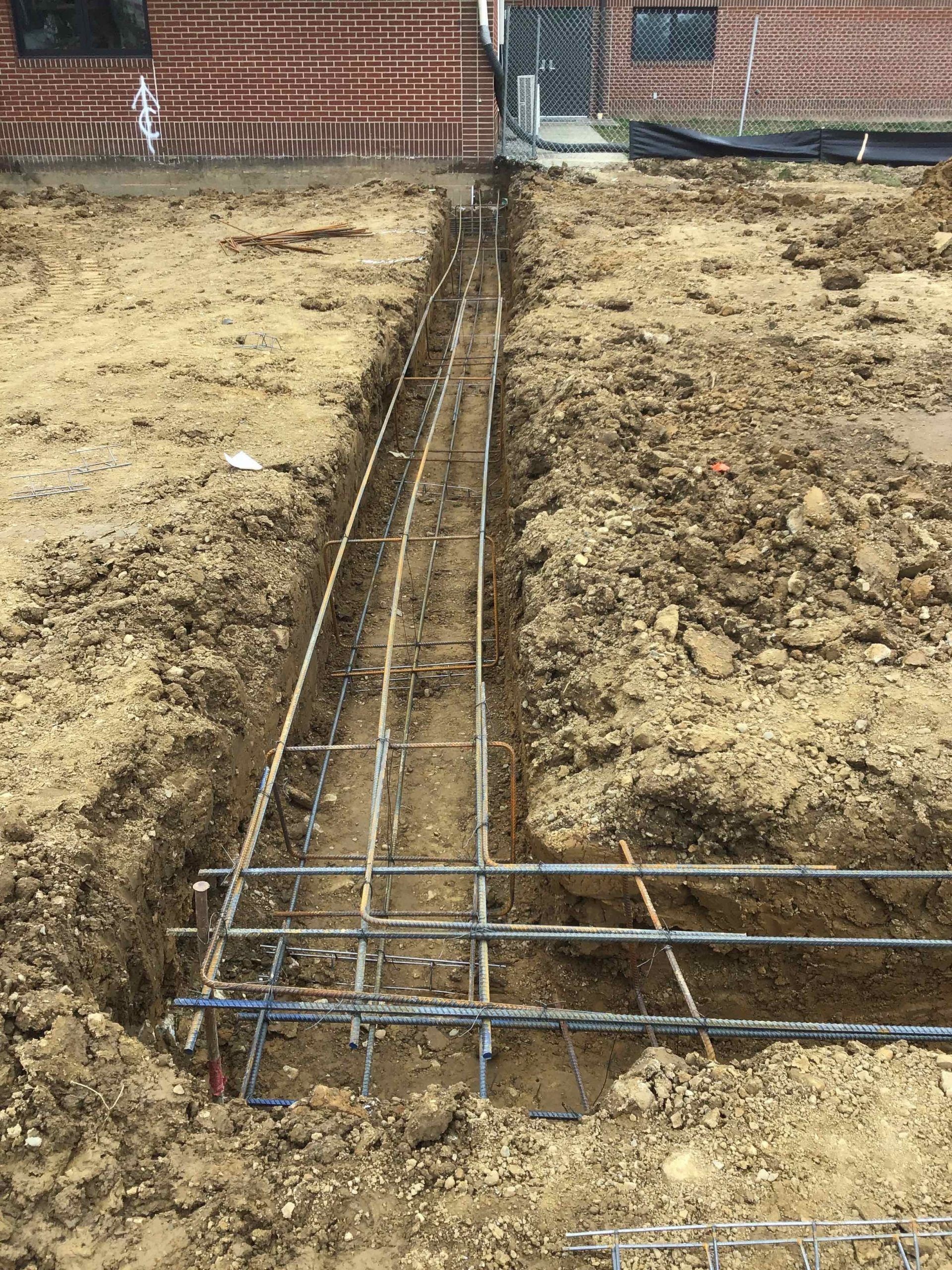 Trench with rebar framework, ready for concrete foundation pour. Construction site setting.