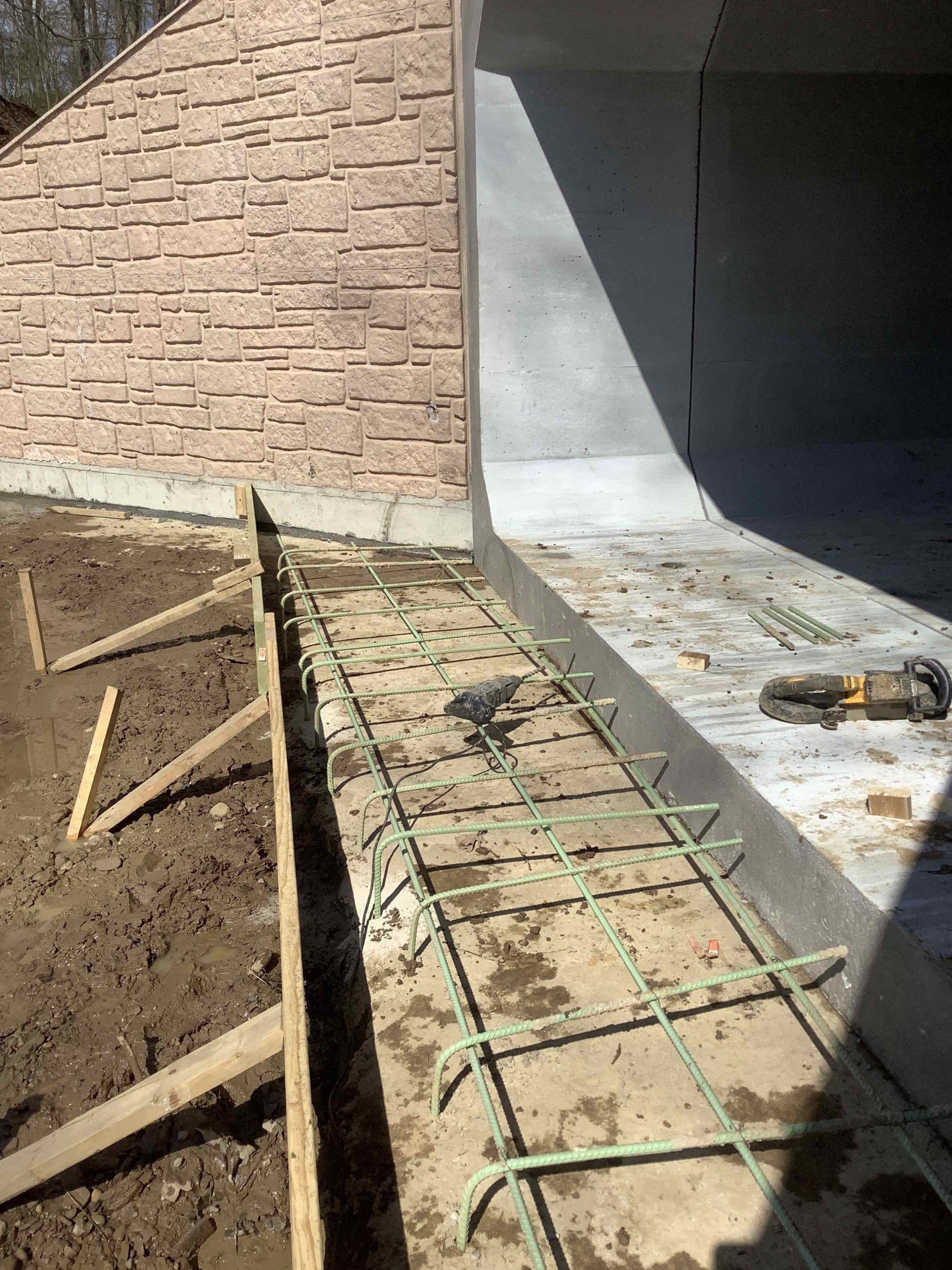 Construction site with concrete forms, rebar, and partially poured concrete next to a brick wall.