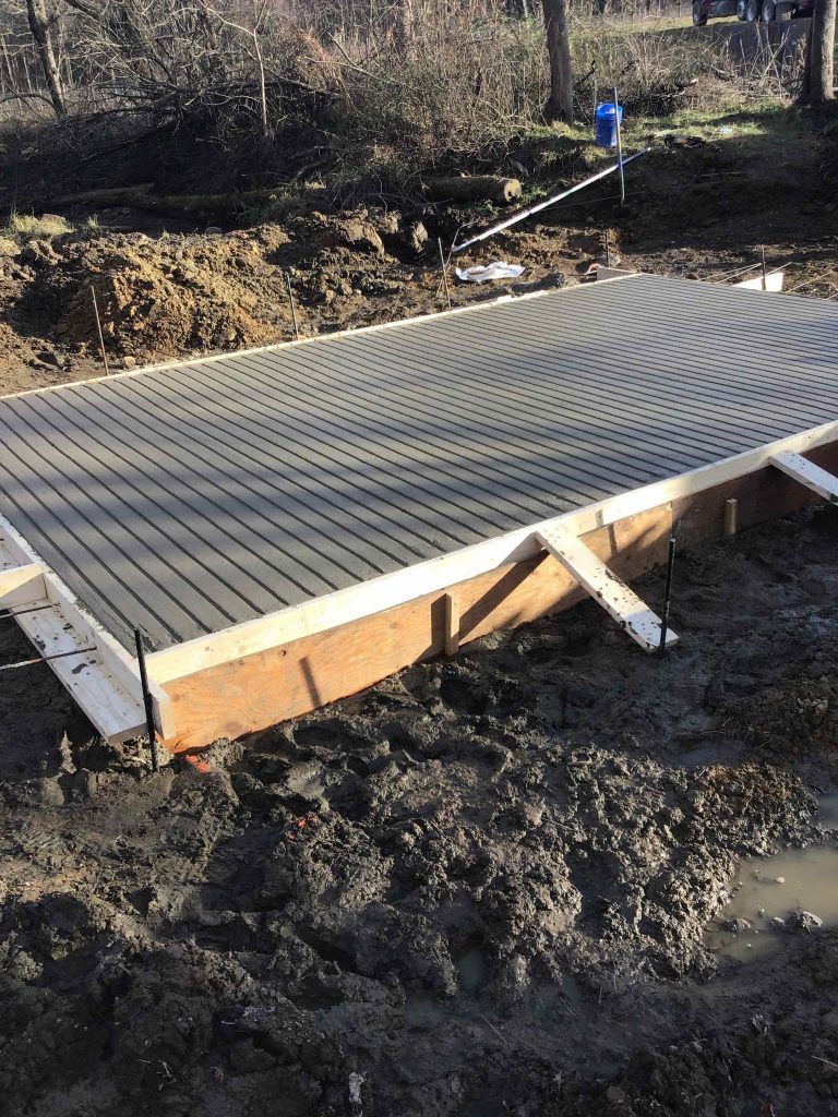 Concrete slab foundation in wooden frame, surrounded by mud.