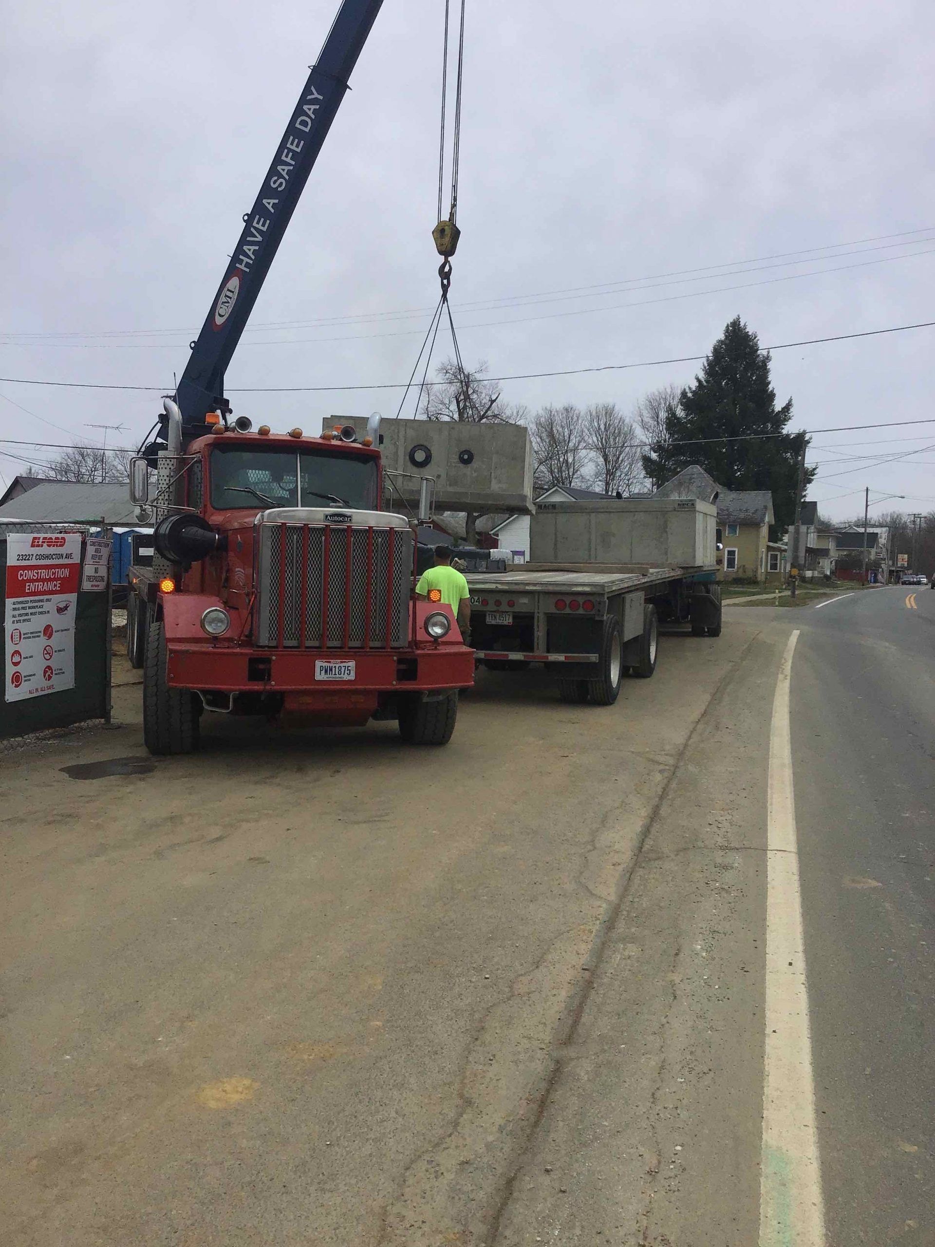 A red crane truck lifting a concrete structure from a flatbed trailer on a street.