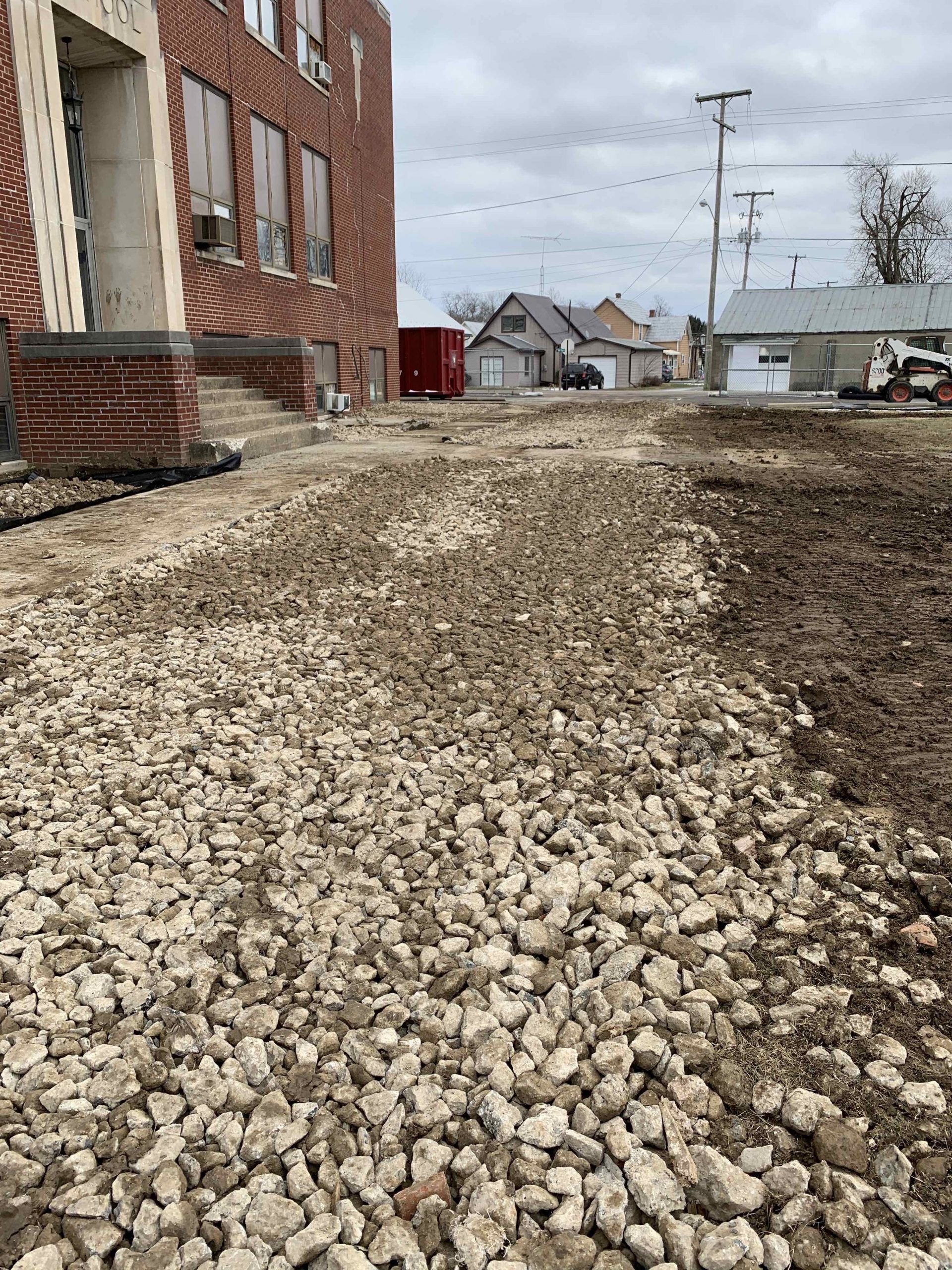 Construction site with gravel pathway, brick building, and cloudy sky.