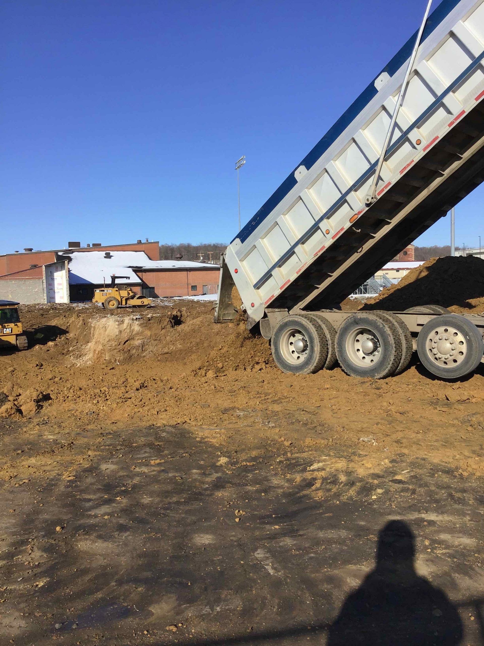 Dump truck unloading dirt on a construction site; blue sky in background.
