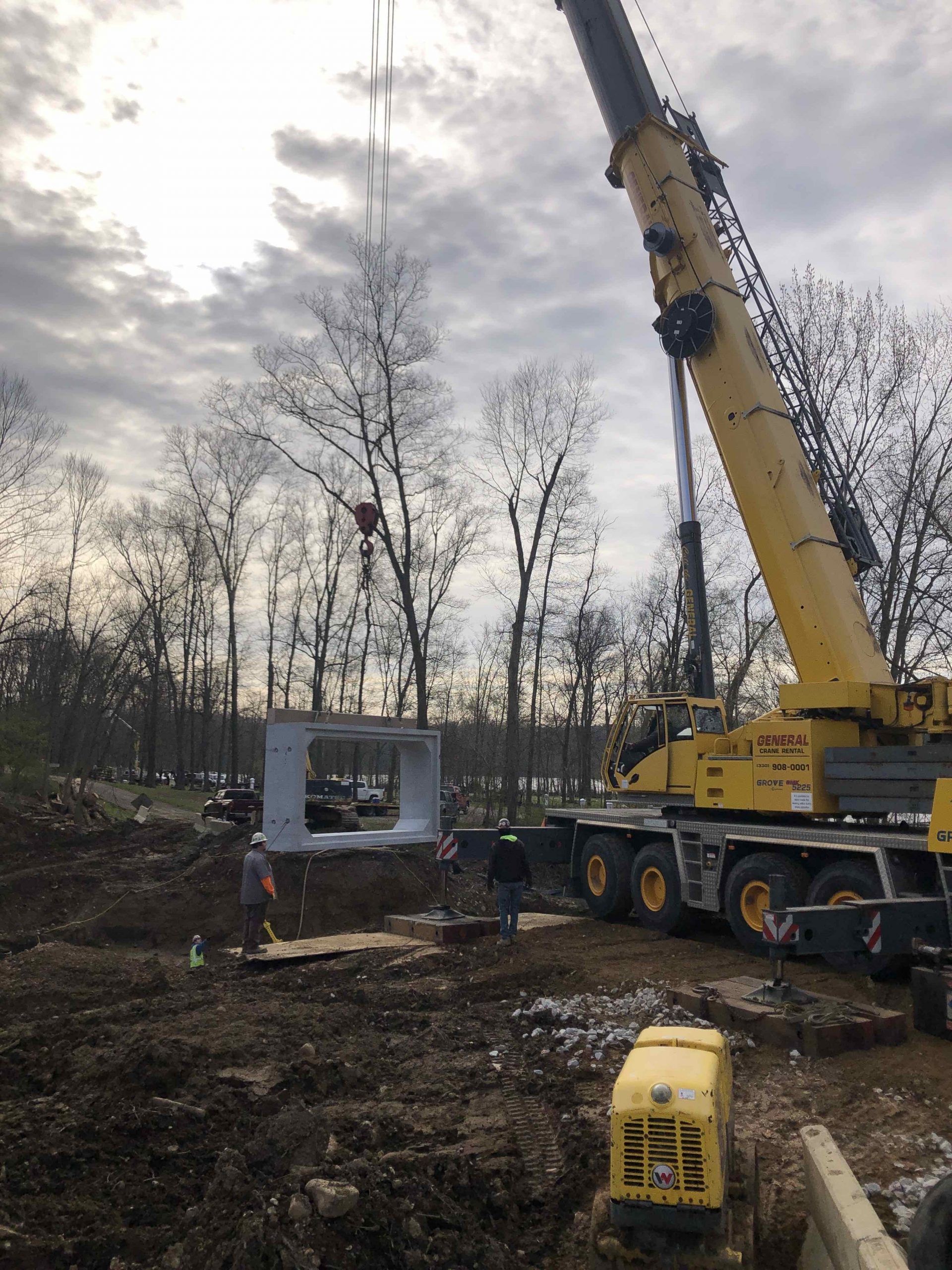 Yellow crane lifting a large, square concrete structure into a construction site.