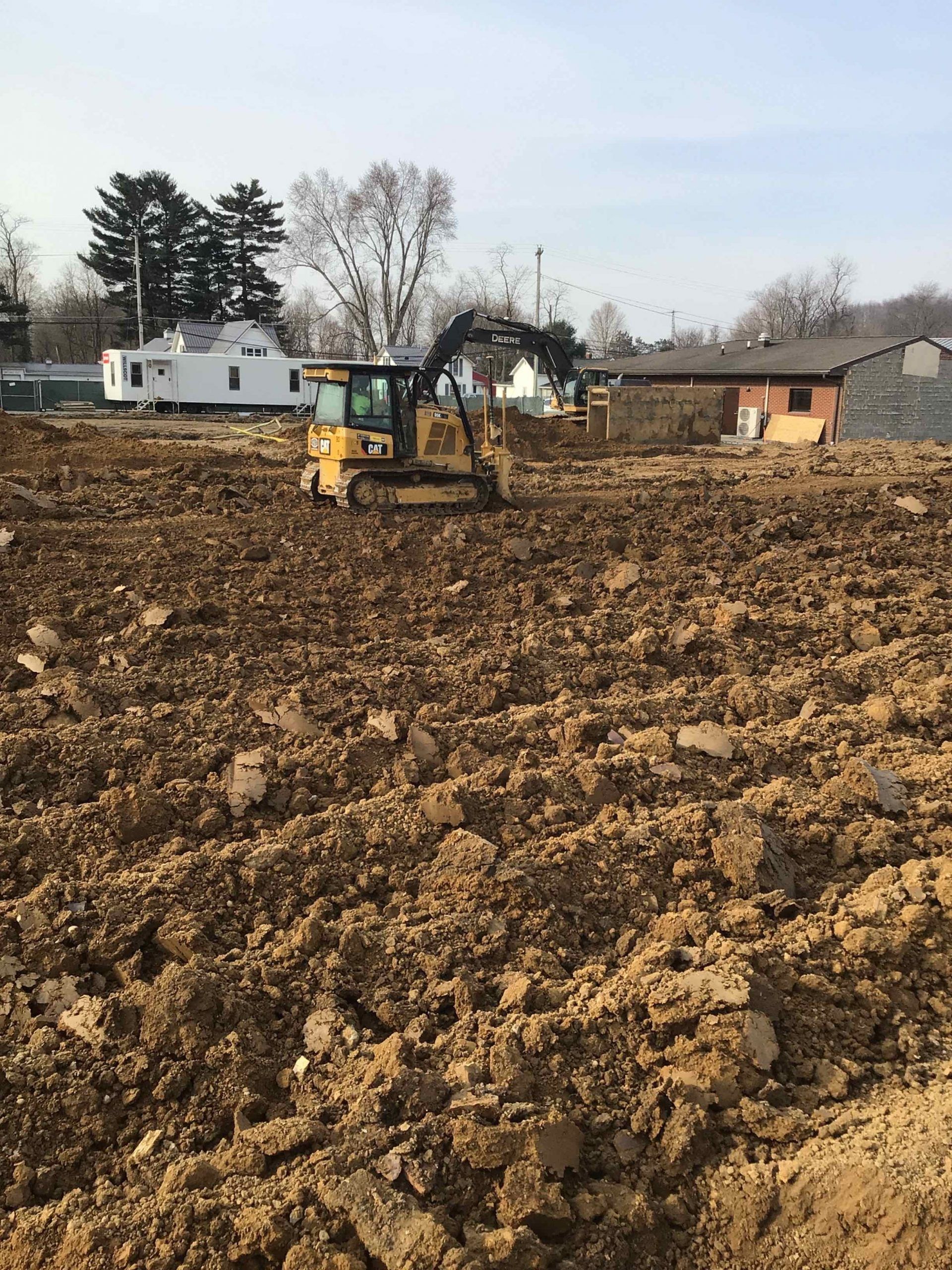 Yellow excavator in a dirt field. Clearing a construction site near buildings.