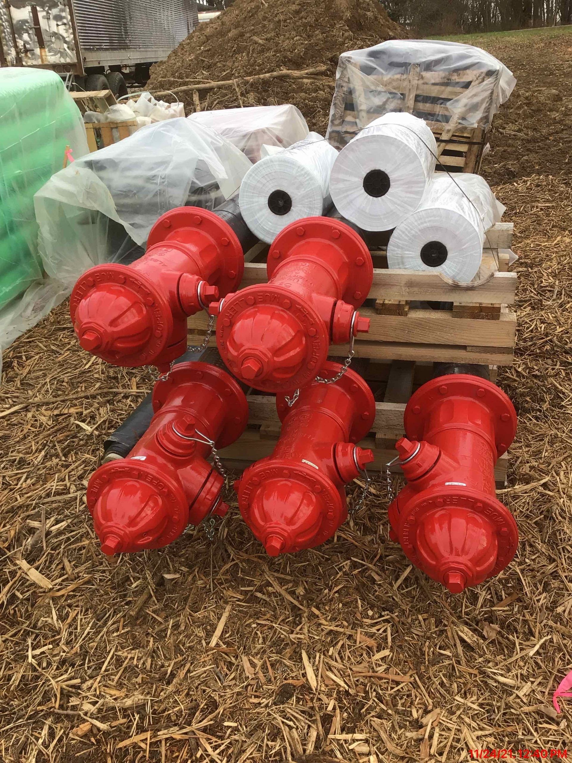 Six red fire hydrants on a wood pallet, with rolls of material in the background.
