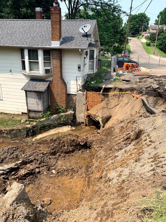 House next to a large excavation site. Dirt and equipment visible.