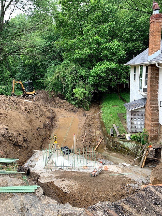 Construction site with excavated ground, foundation, and house. Mini excavator in the background.