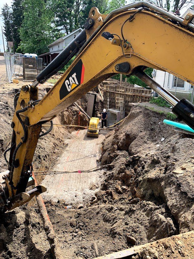 Yellow CAT excavator digging a trench, small tractor in the distance, construction site.