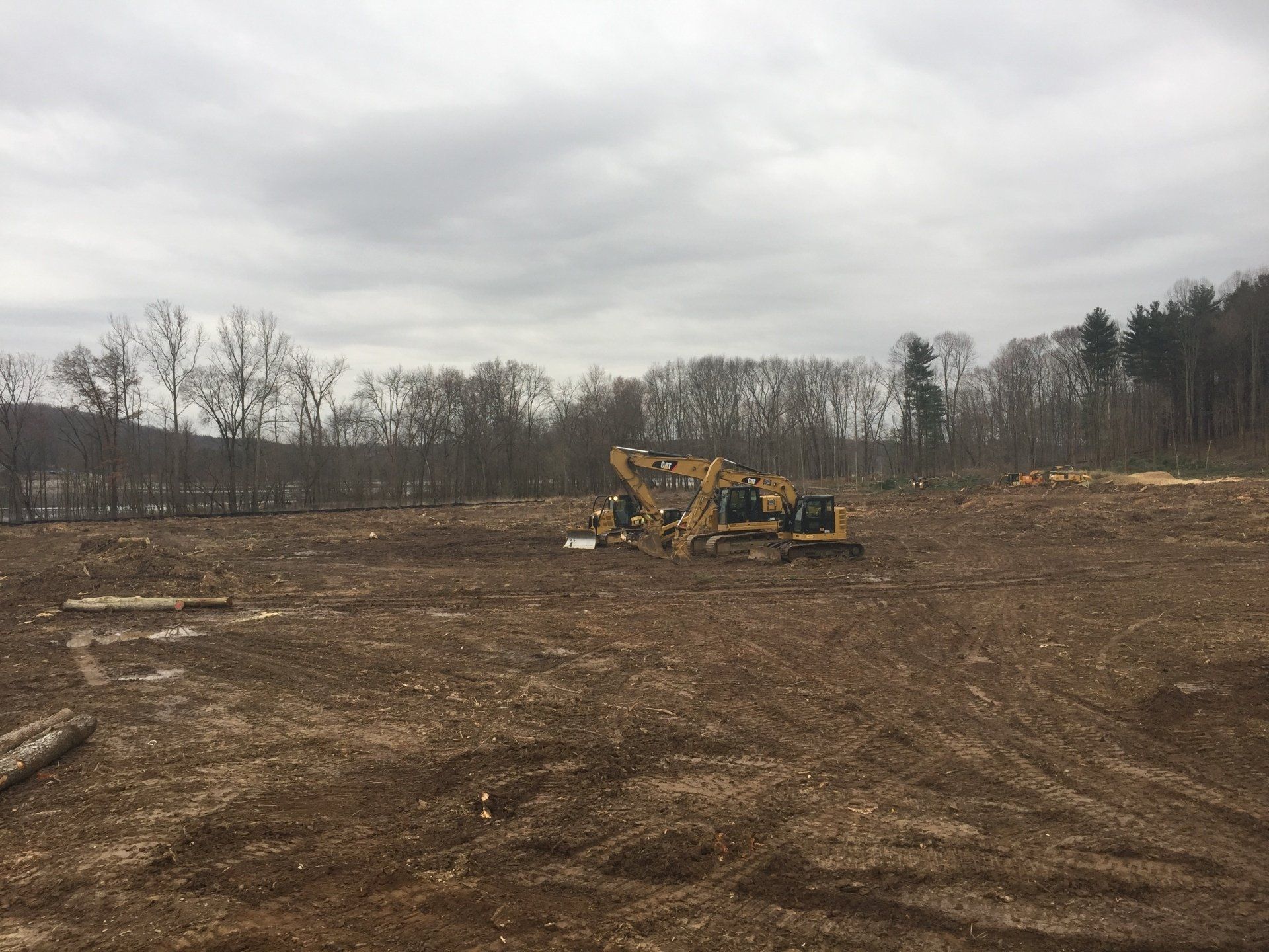 Construction site with heavy machinery on a cleared field. Trees in the background, cloudy sky.
