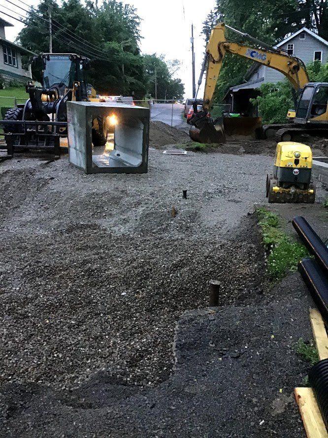 Construction site with heavy machinery, gravel, and a concrete culvert.