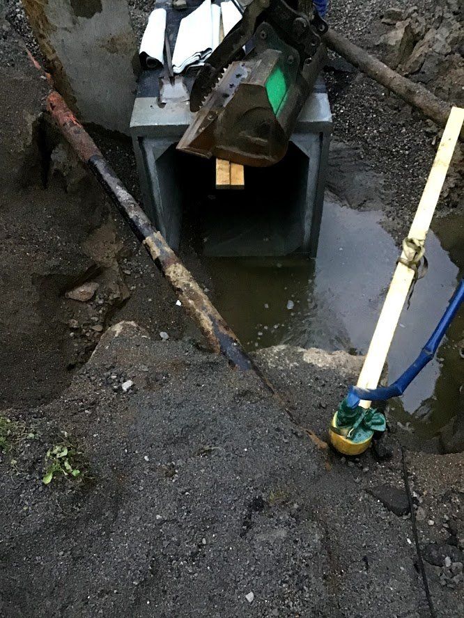 Construction site with a concrete box culvert. Dirt, water, machinery and tools visible.