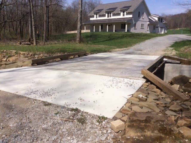 Newly constructed concrete bridge over a small creek, leading to a two-story house.