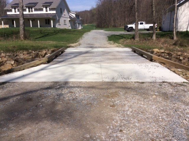 Gravel driveway with concrete bridge leading to a house, with a truck parked in the distance.