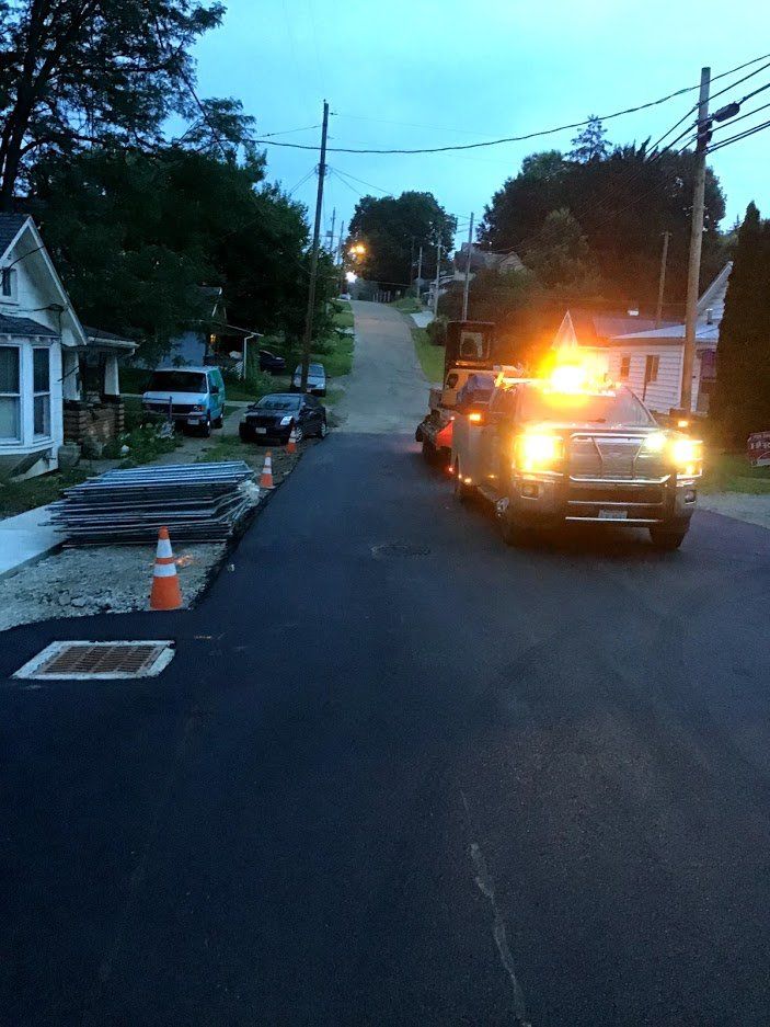 Tow truck on newly paved road; construction cones and houses line the street.