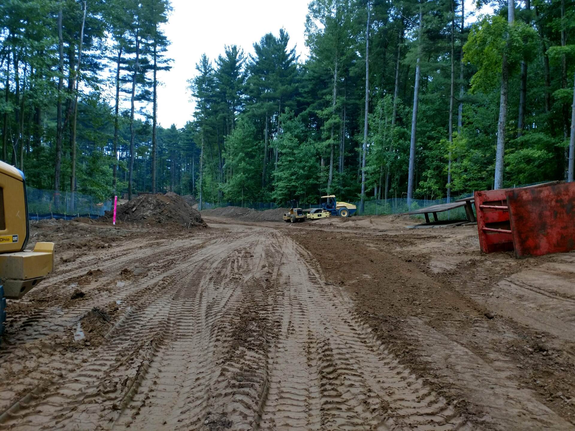 Construction site: bulldozers on muddy ground, trees in background, and a red dumpster.