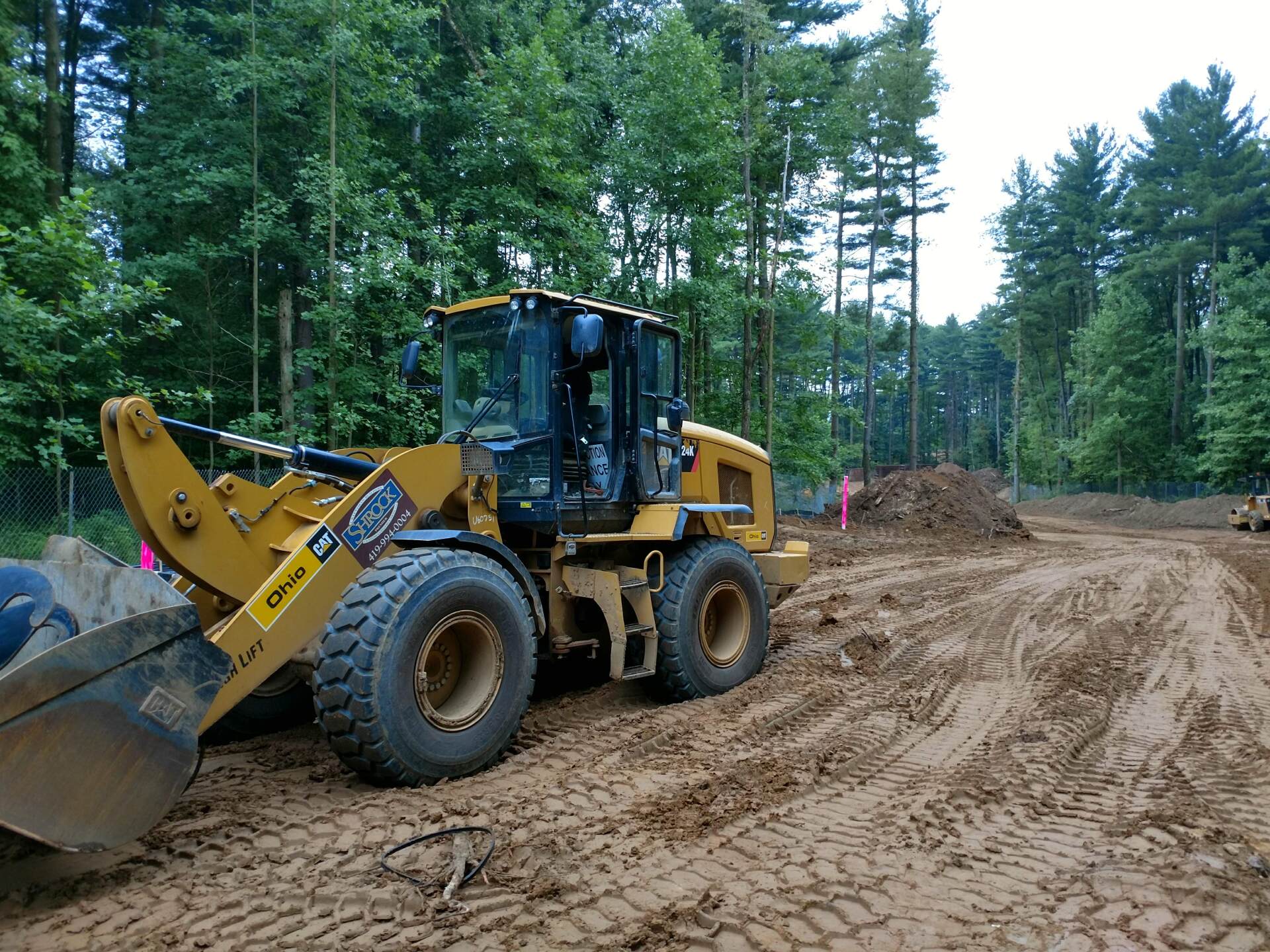 Yellow construction loader on muddy ground, clearing land near trees.