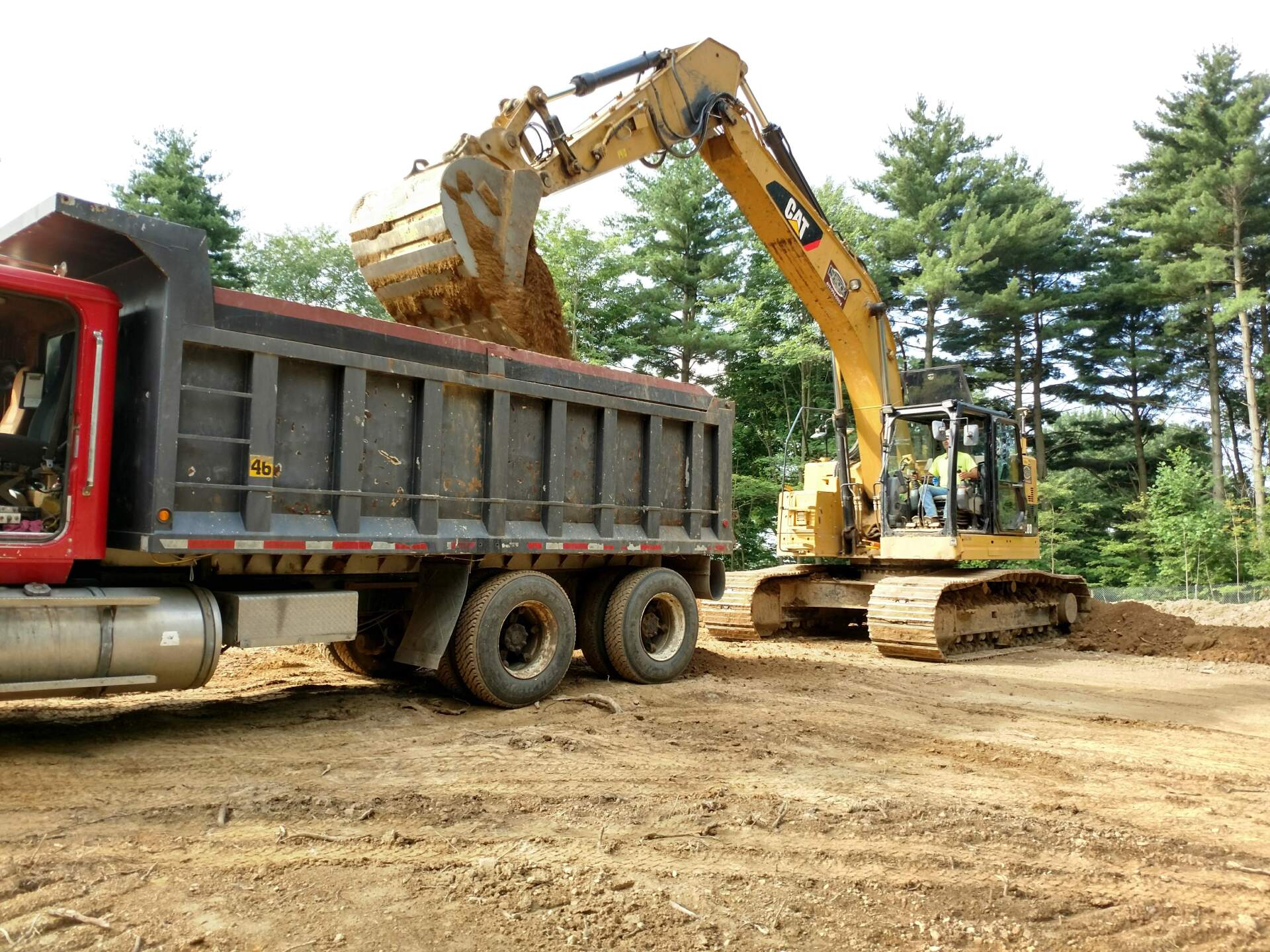 Excavator loading dirt into a red dump truck in a construction site.