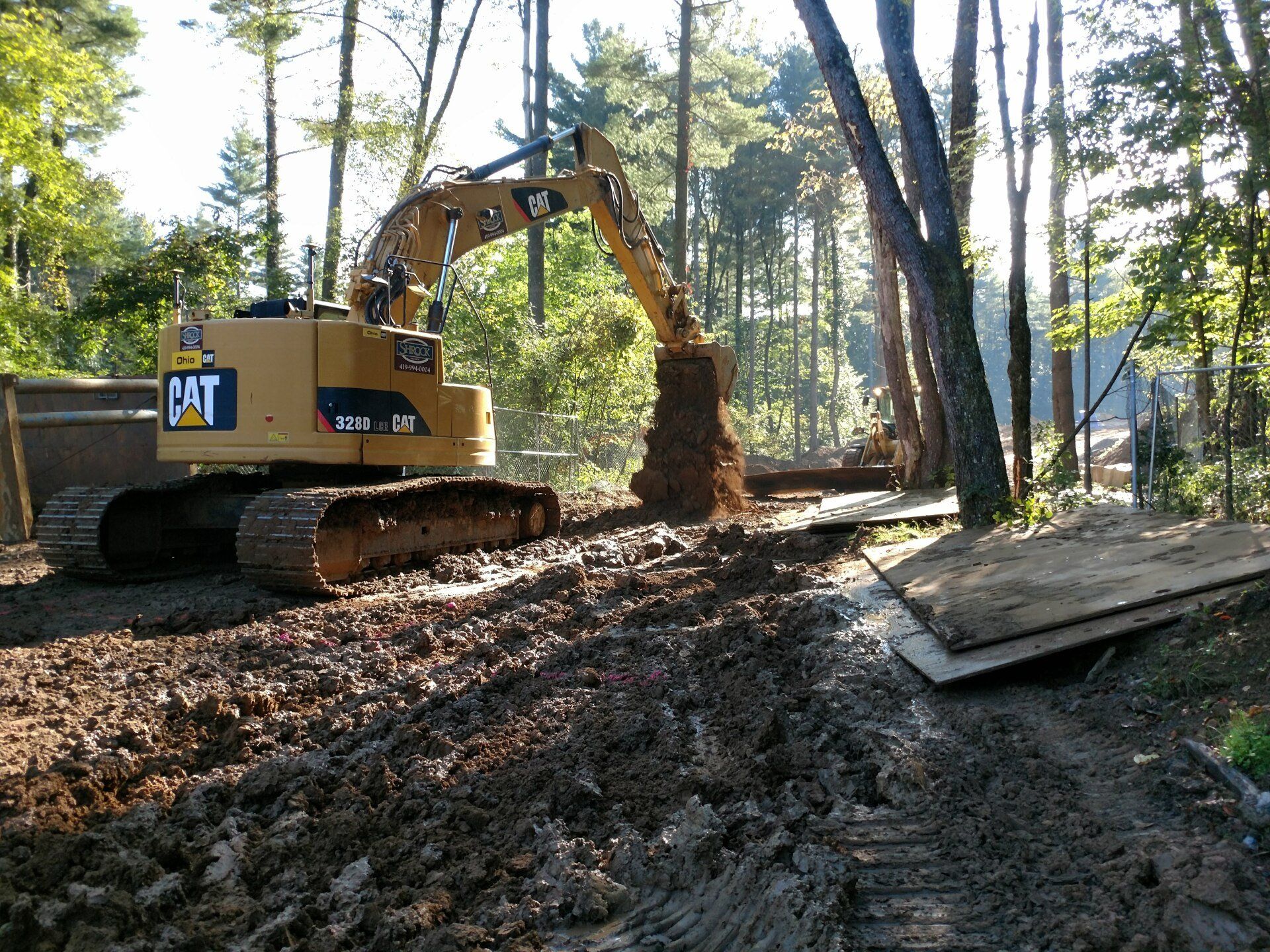Yellow Caterpillar excavator digging in muddy terrain, surrounded by trees.