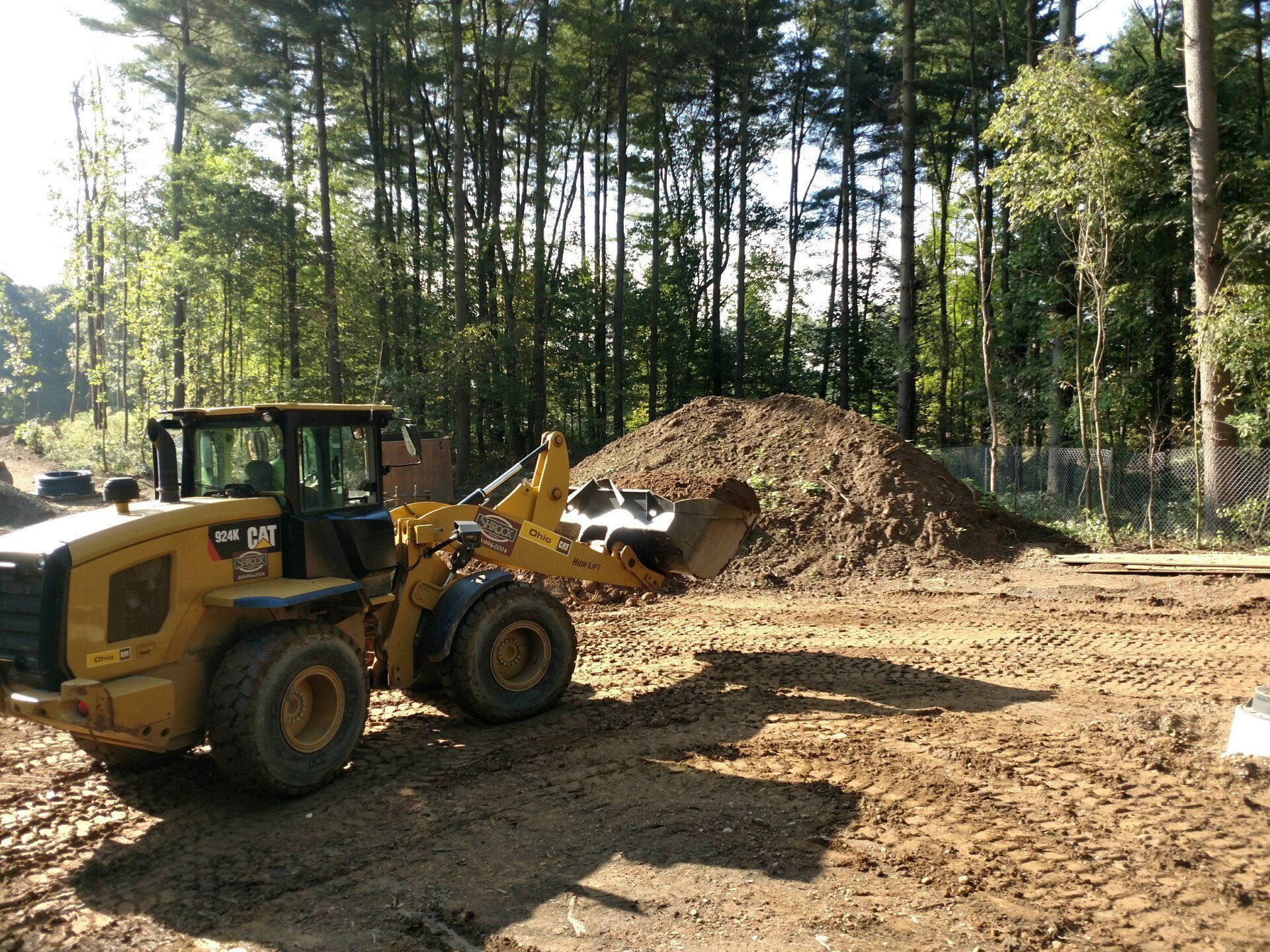 Yellow loader moving dirt near a pile and a forest.
