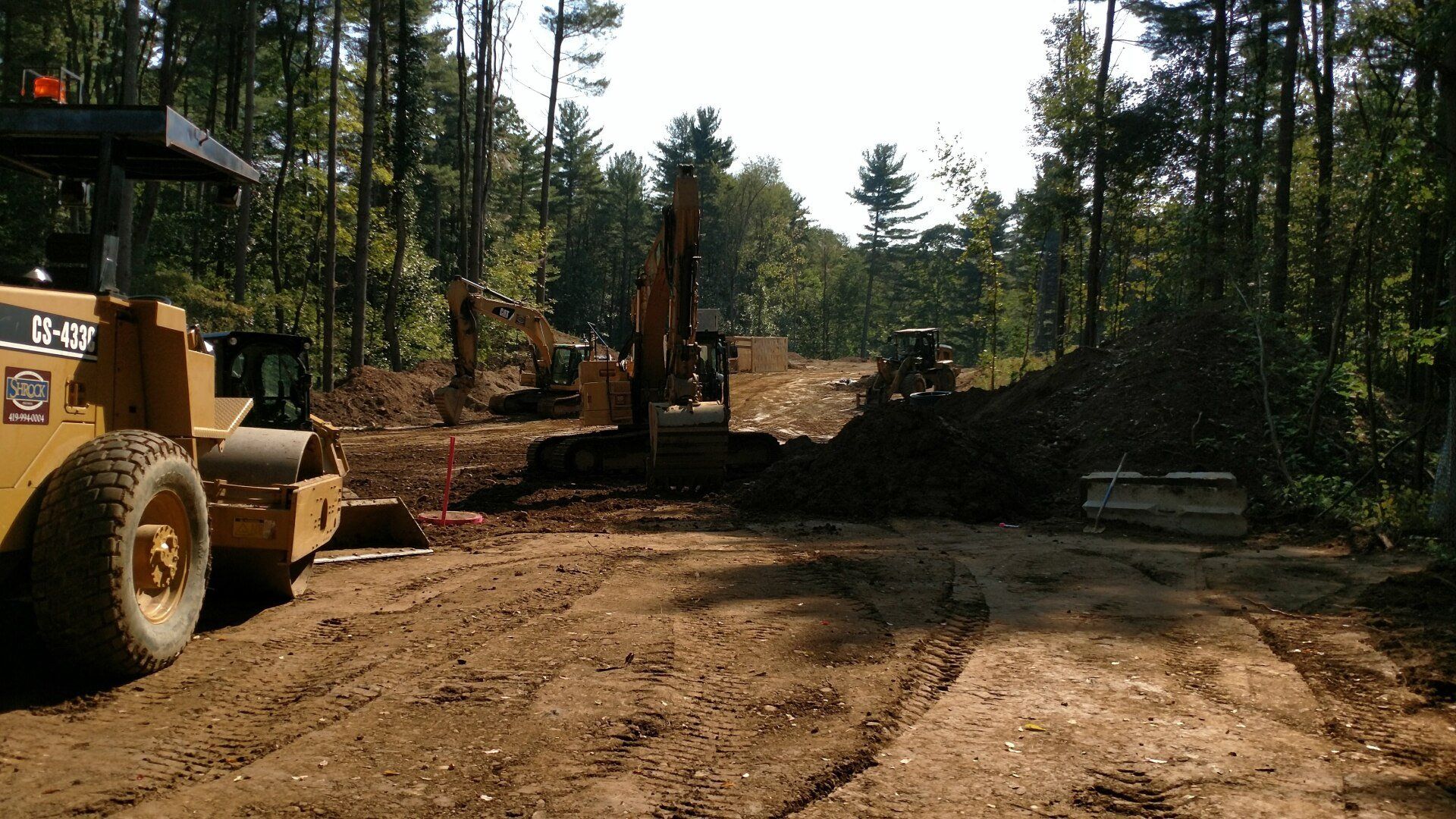 Construction site with heavy machinery like a roller and excavator. Trees in the background.