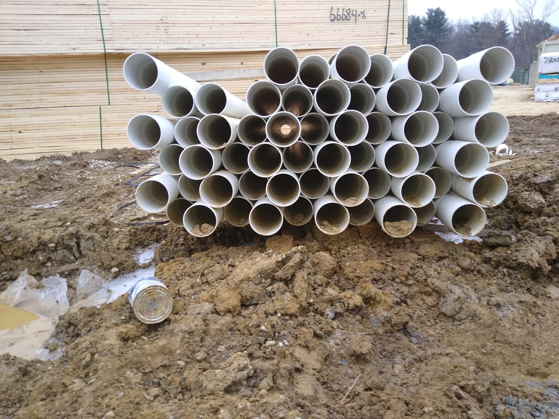 Stack of white PVC pipes on muddy ground at a construction site.