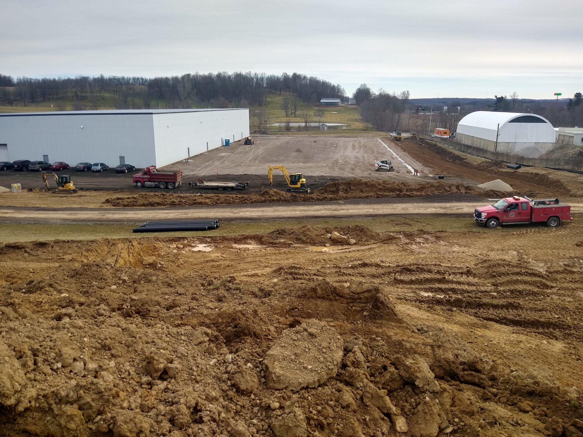 Construction site with heavy machinery, trucks, and a large building under cloudy skies.