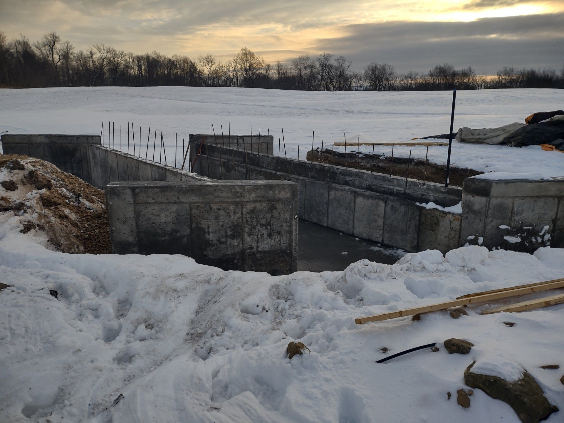 Concrete foundation under construction in snowy field; cloudy sky in background.