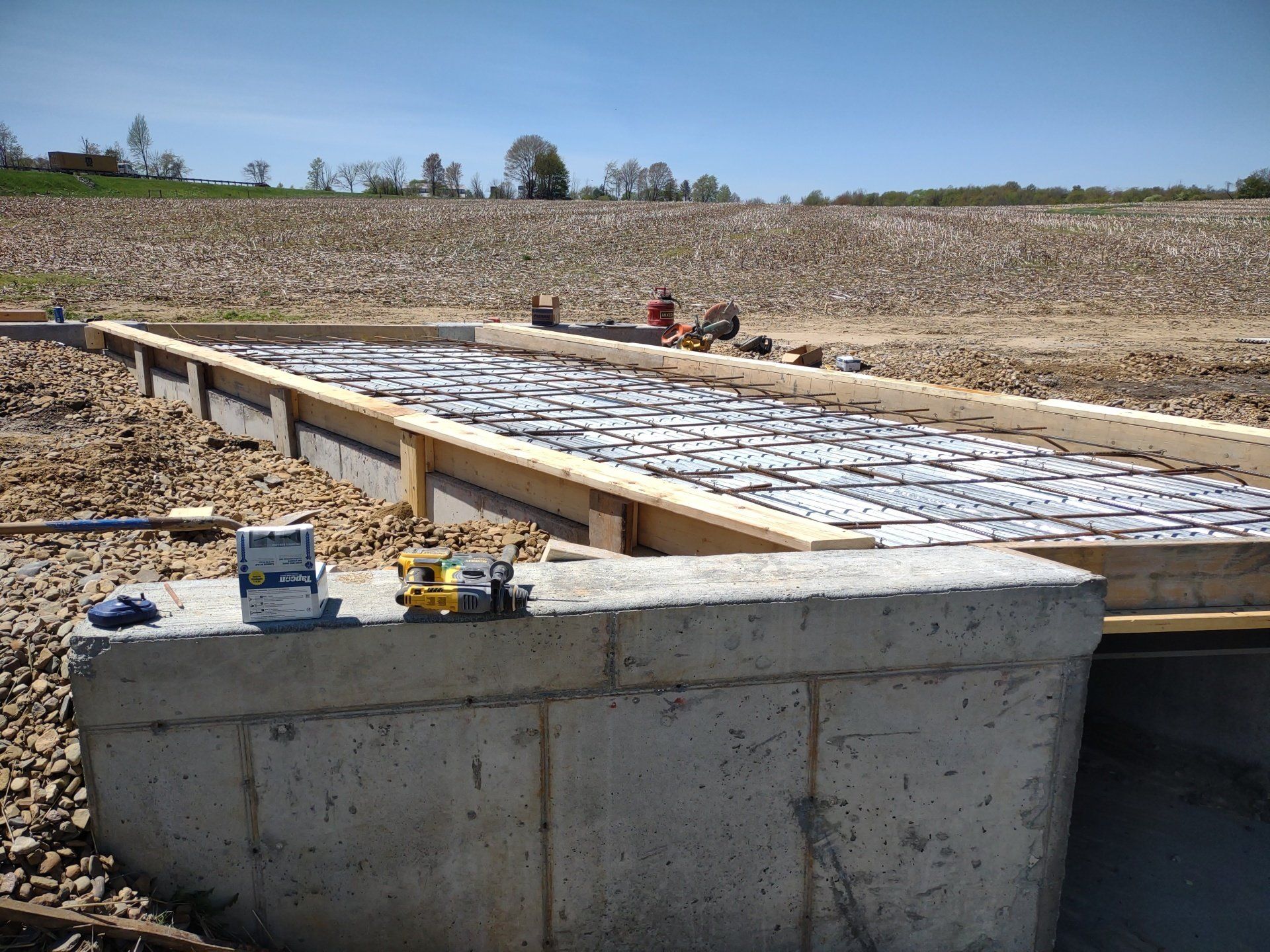 Construction site: concrete blocks and wooden frame with objects, field in background.