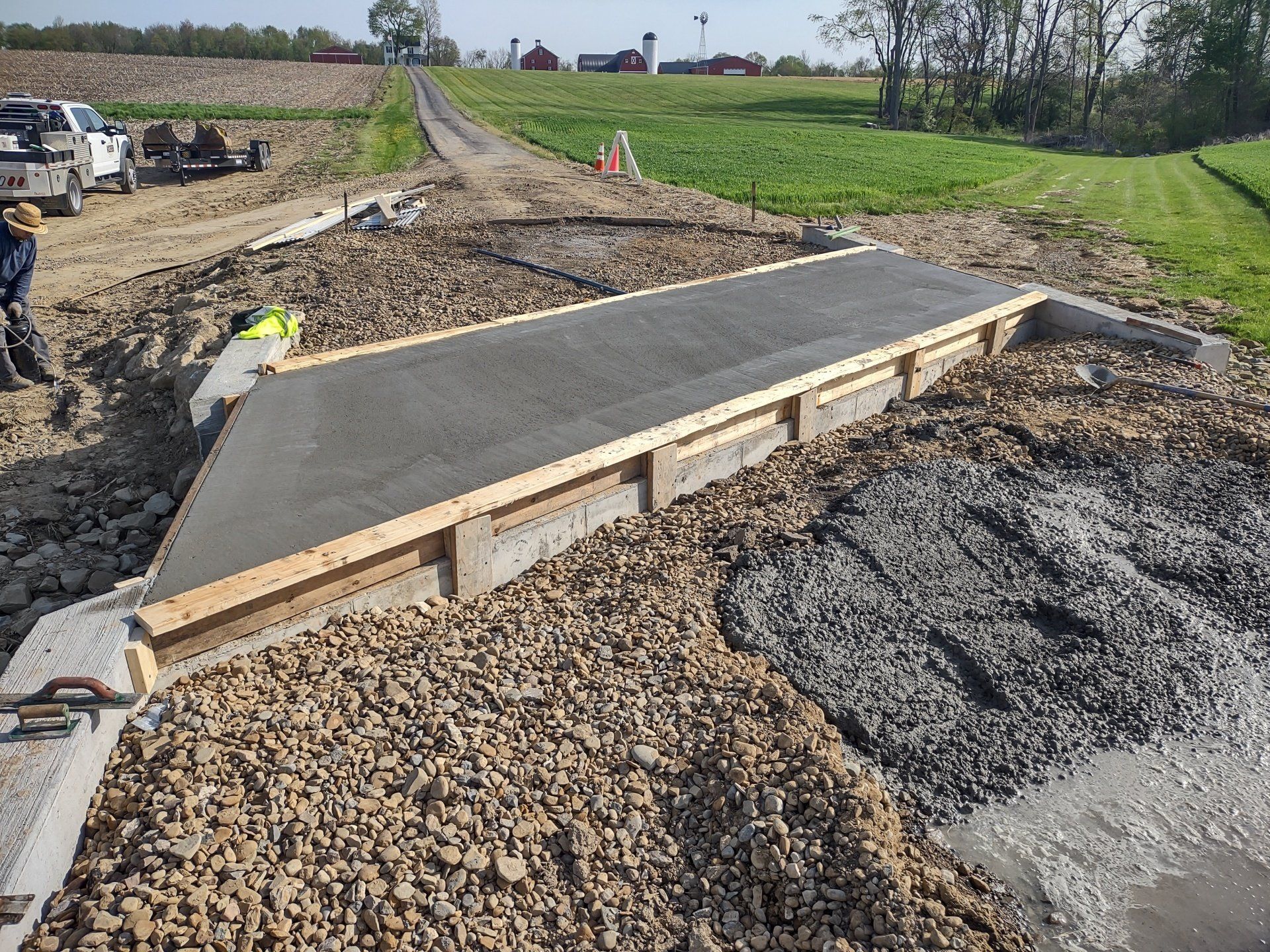 Concrete ramp construction in a rural setting, surrounded by gravel and workers.