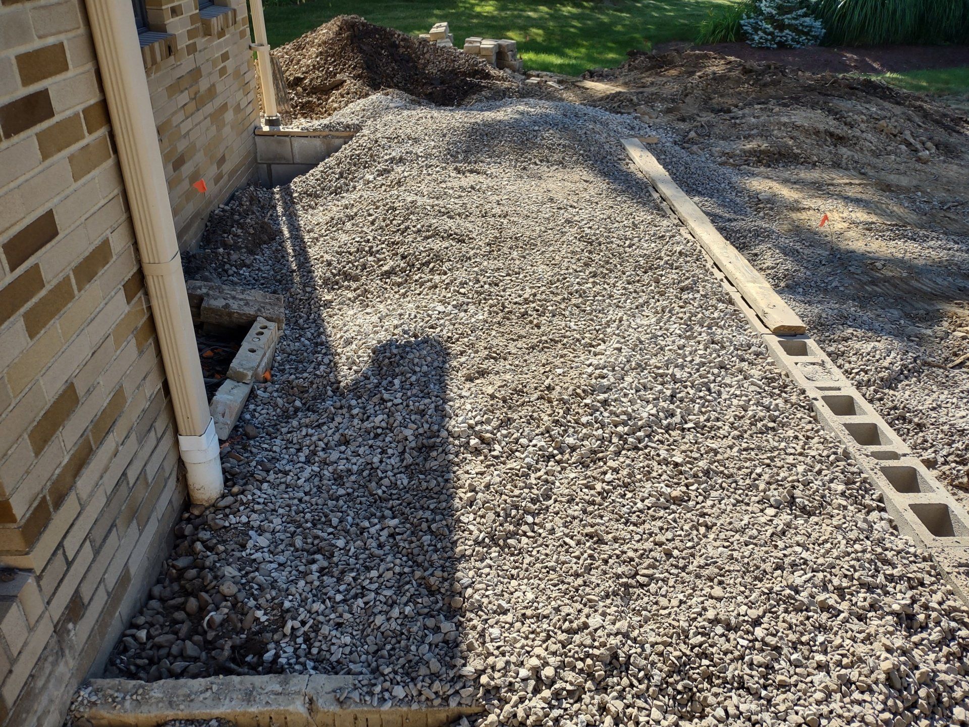 Gravel pathway under construction next to a brick building. Wooden boards and concrete blocks are present.
