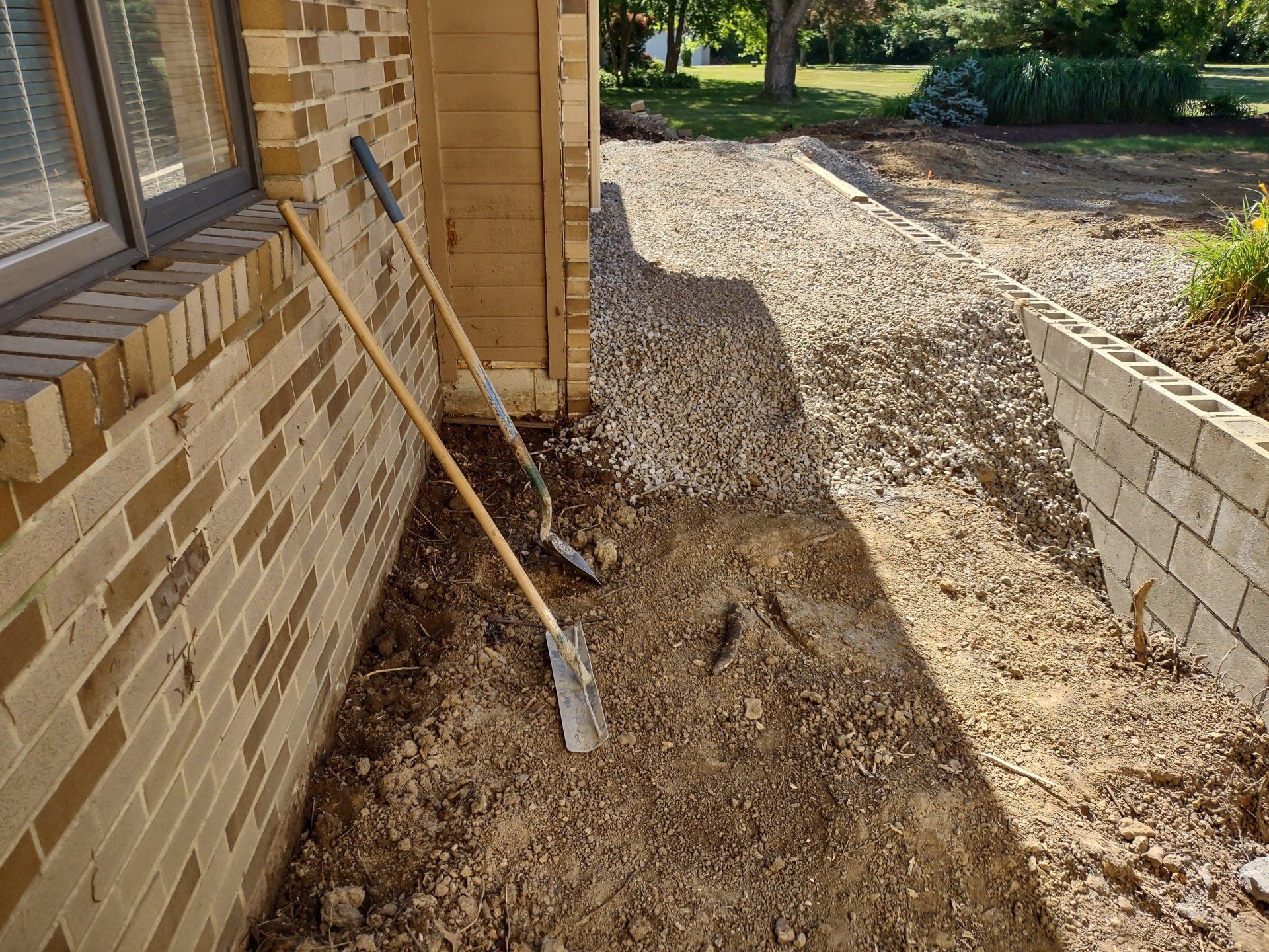 A gravel path under construction along a brick wall, with tools leaning against the wall.