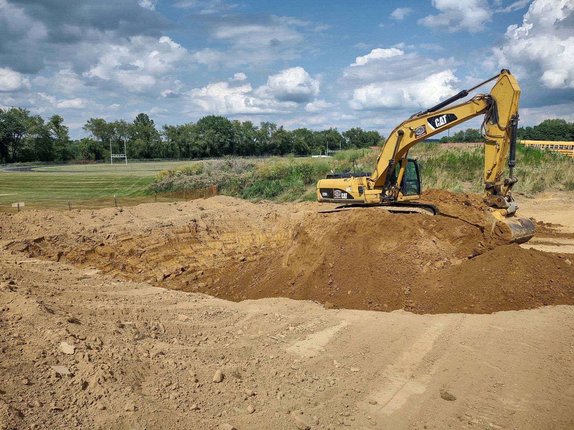 Yellow Caterpillar excavator digging earth on a construction site under a cloudy sky.