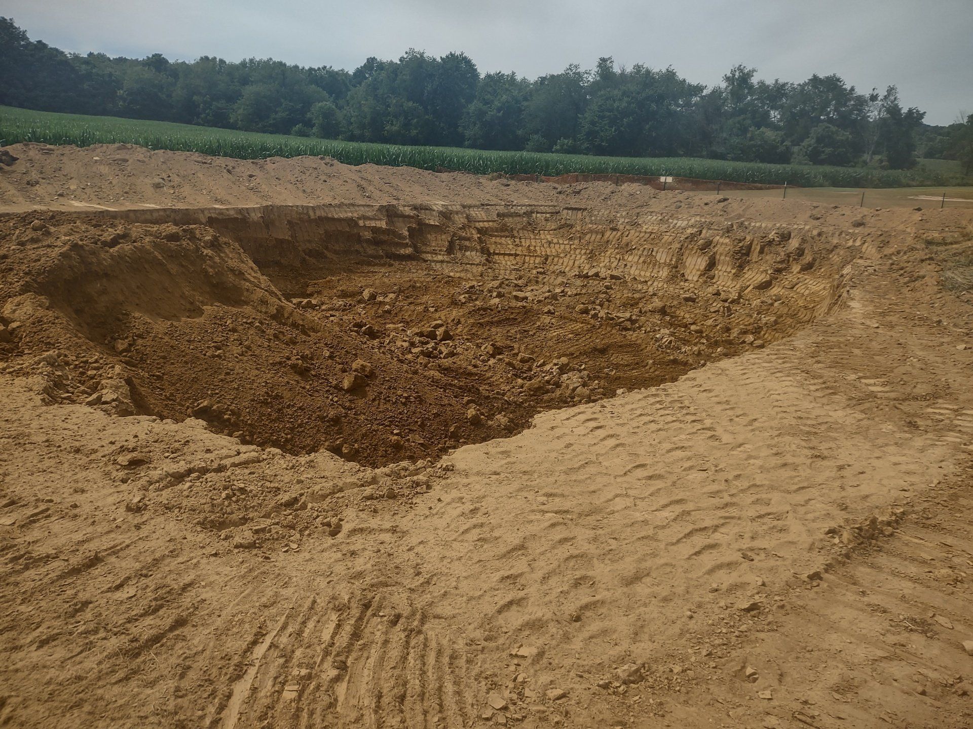 Excavated earth in a field, showing a large hole and surrounding piles of dirt.
