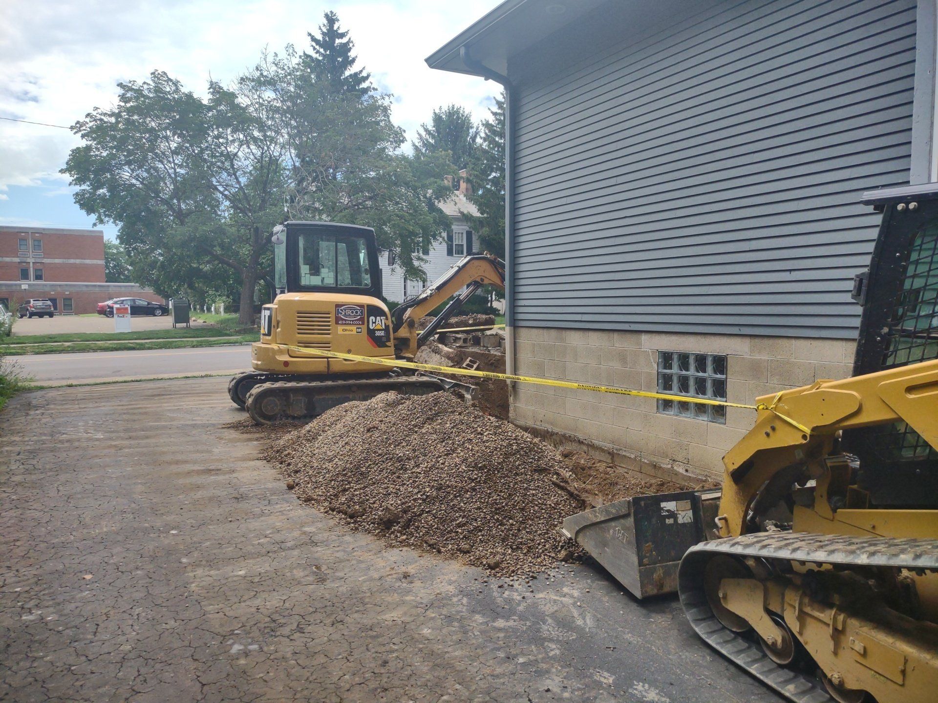 Yellow construction equipment beside a building with a pile of gravel. Caution tape is visible.