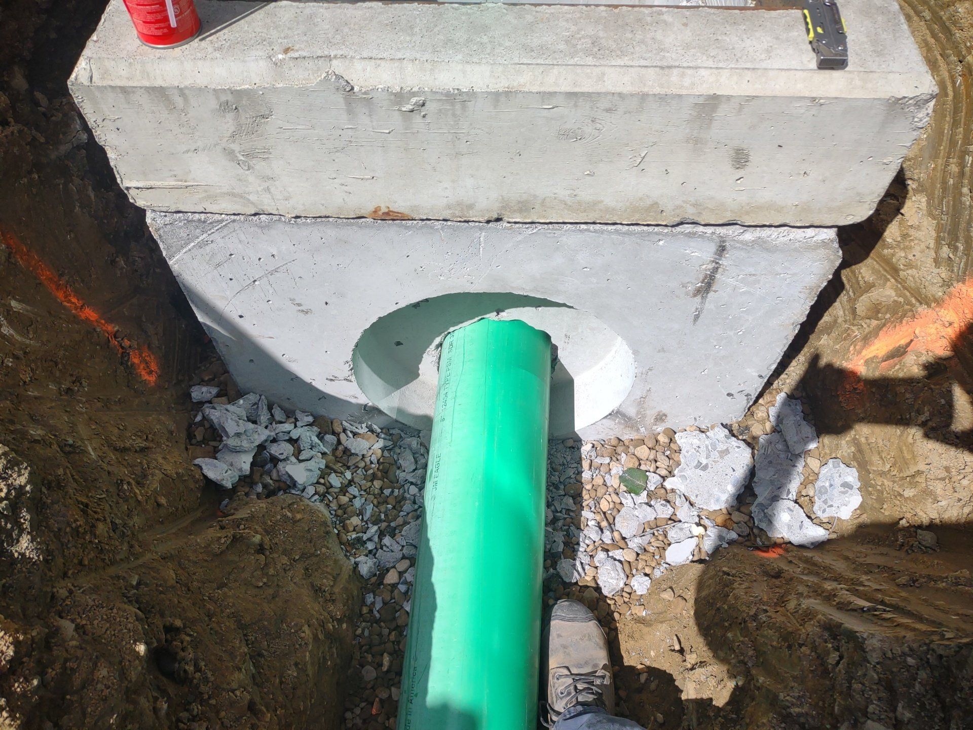 Green pipe entering a concrete structure in a construction setting.
