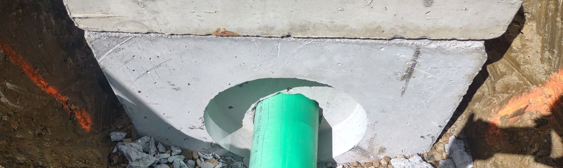 Green pipe exiting a concrete structure. Orange markings on the ground.