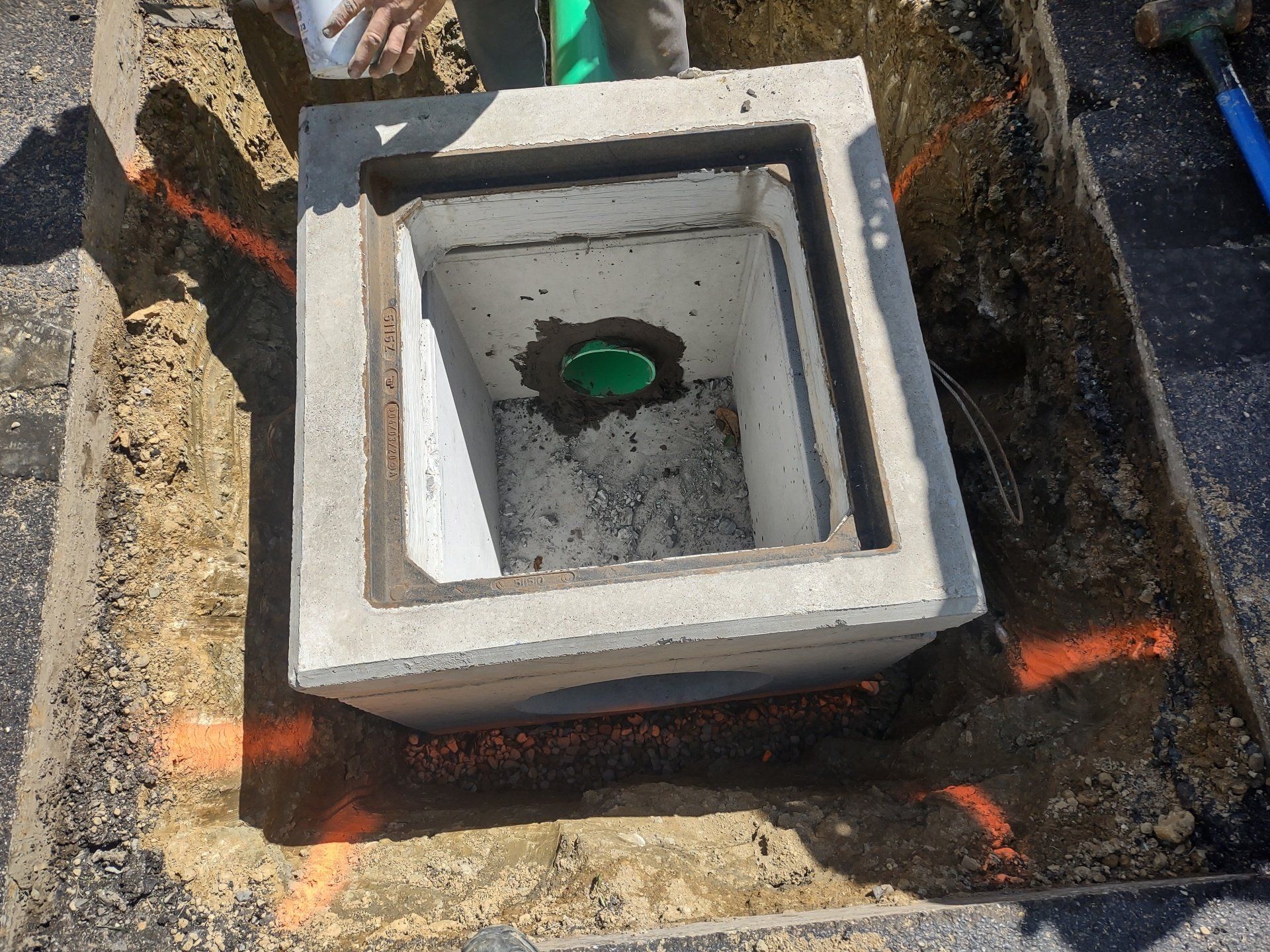 Open concrete drain, green pipe visible inside, marked on asphalt.