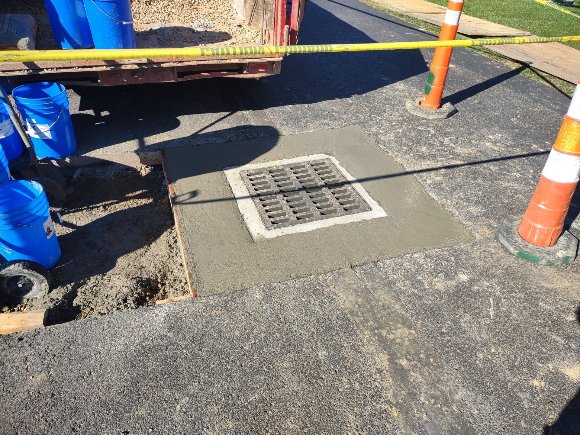 New concrete surrounding a storm drain. Barricade tape and cones indicate a work zone.